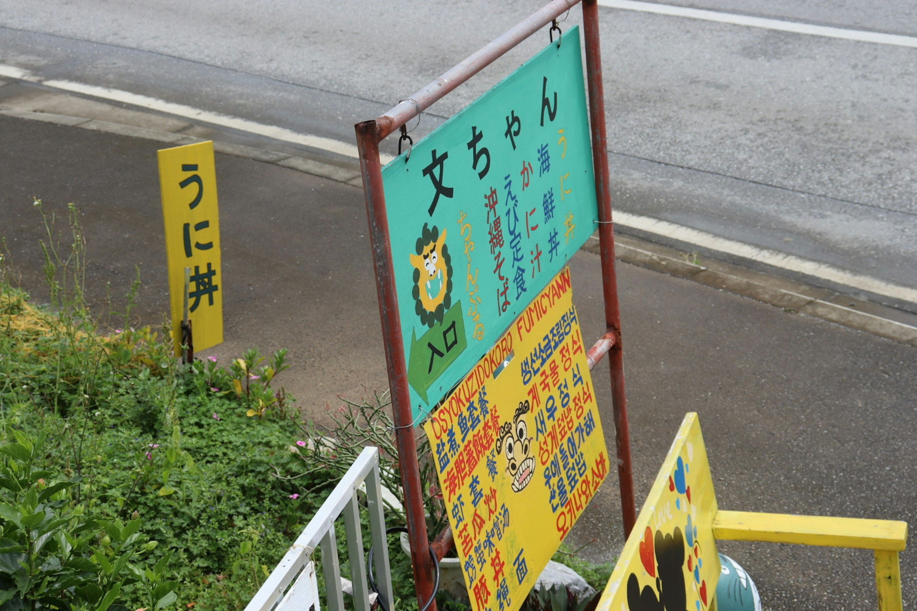 道路沿いの飲食店の看板があり、緑色の背景にメニューが書かれている