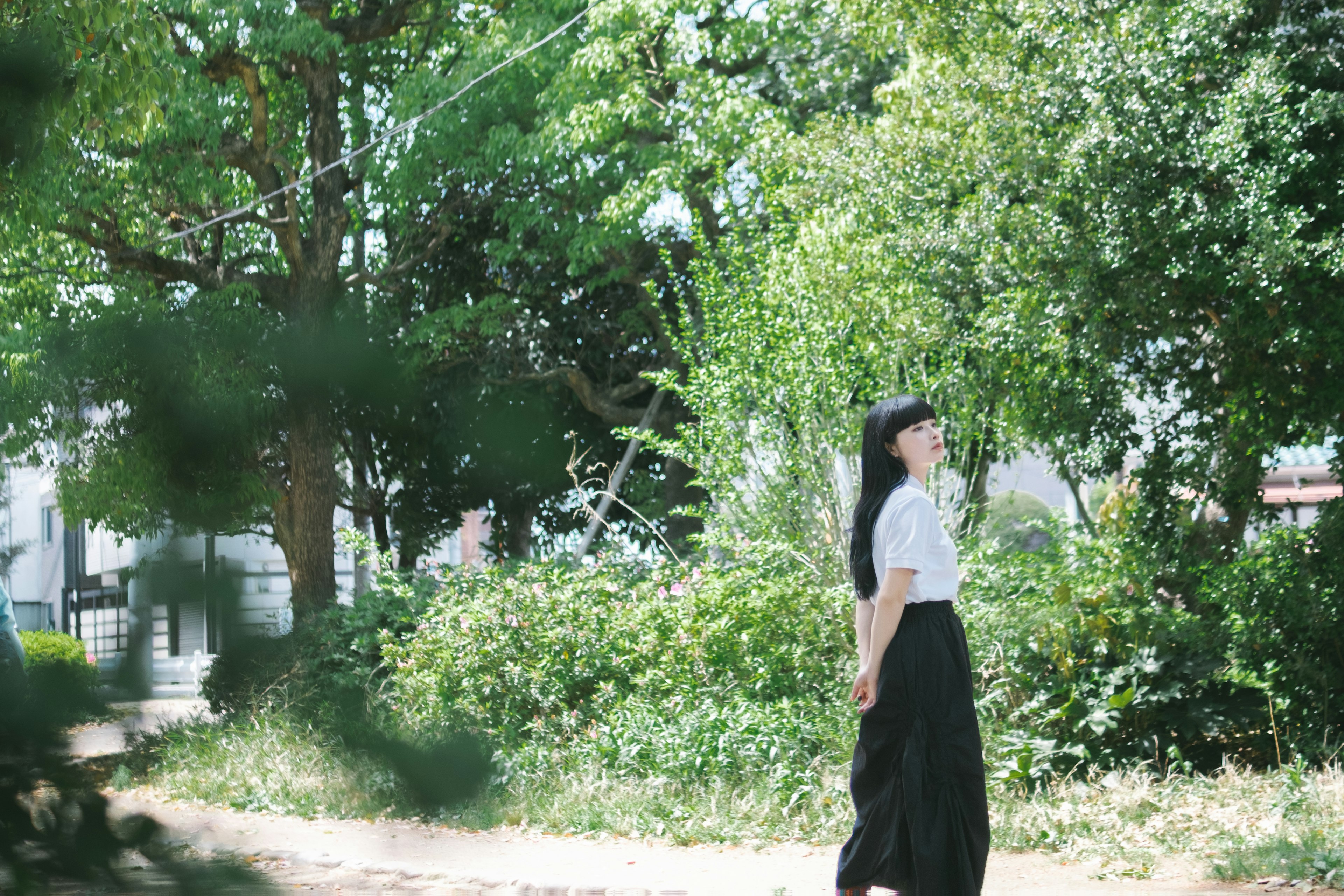 Une femme marchant parmi des arbres verts portant un haut blanc et une jupe noire