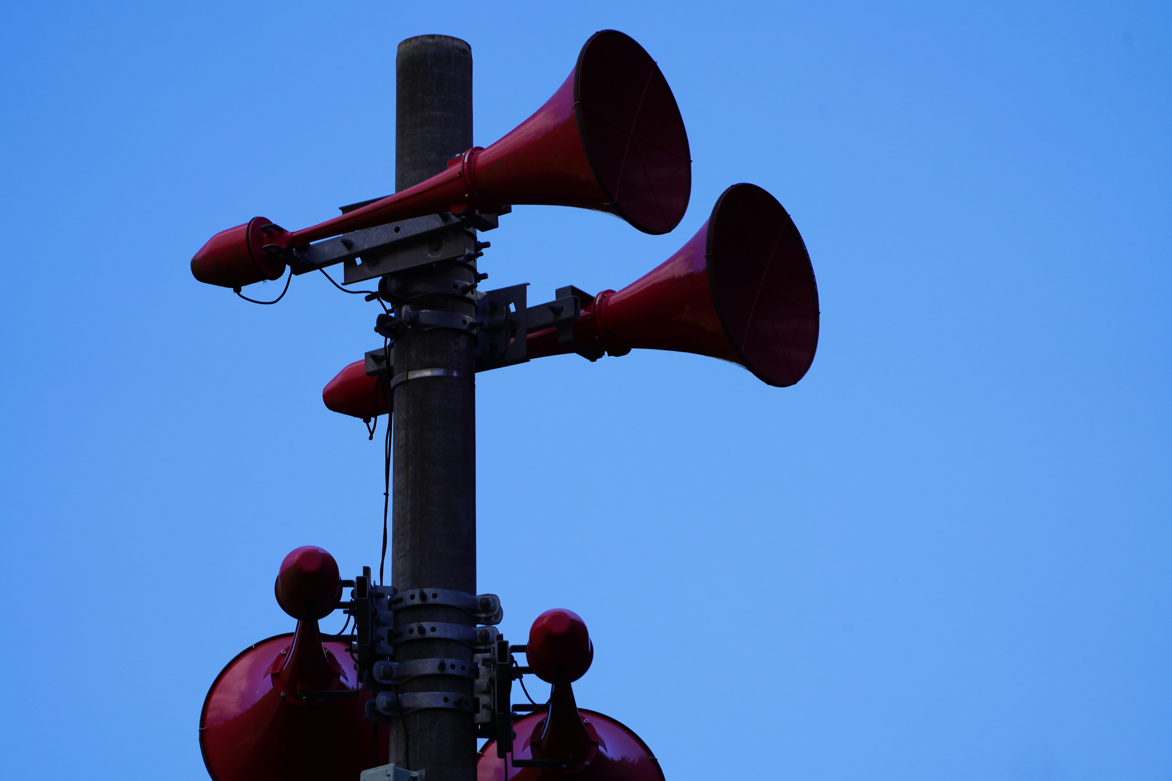 Altavoces en forma de bocina rojos montados en un poste bajo un cielo azul