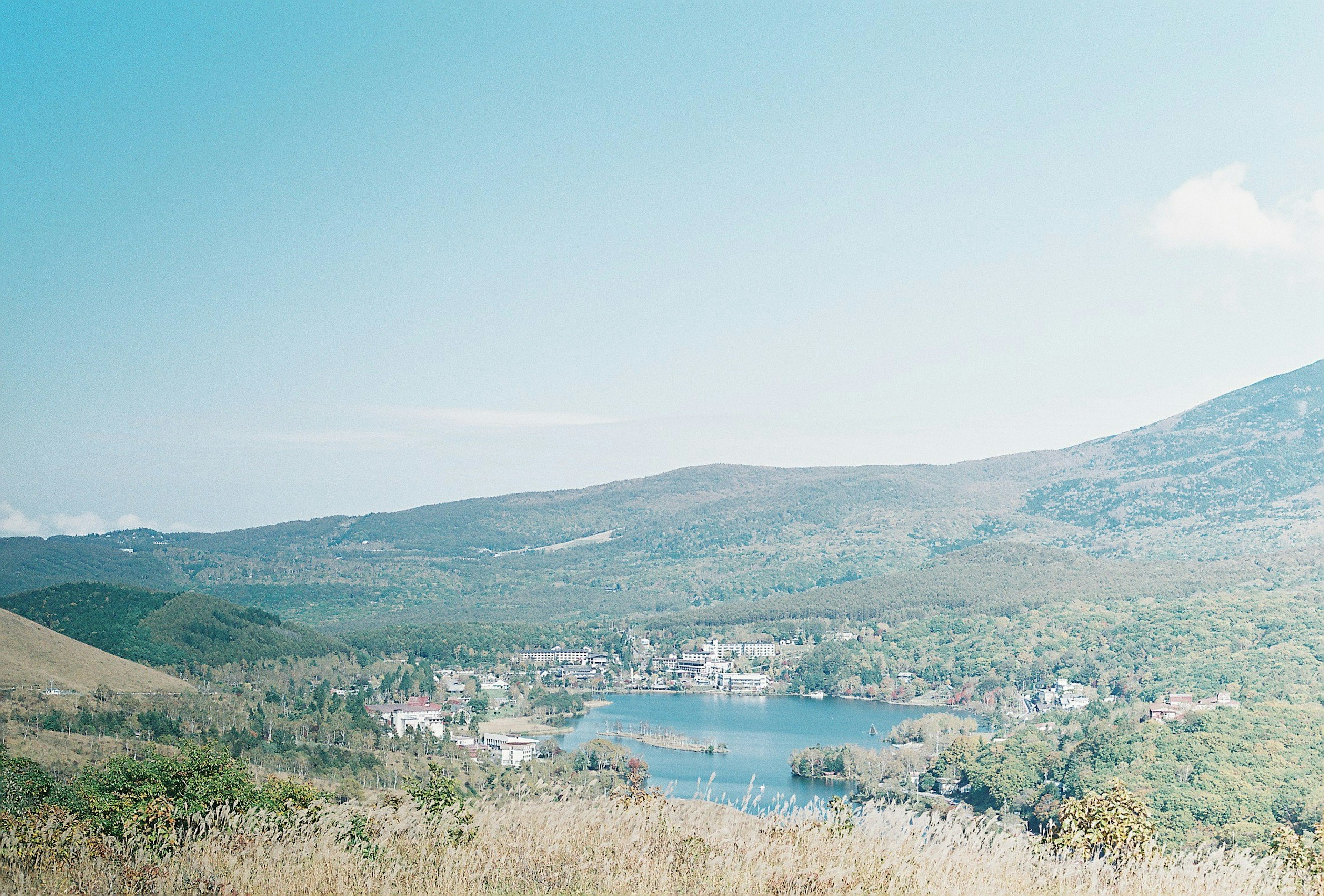 Un pueblo junto a un lago rodeado de montañas verdes bajo un cielo azul claro