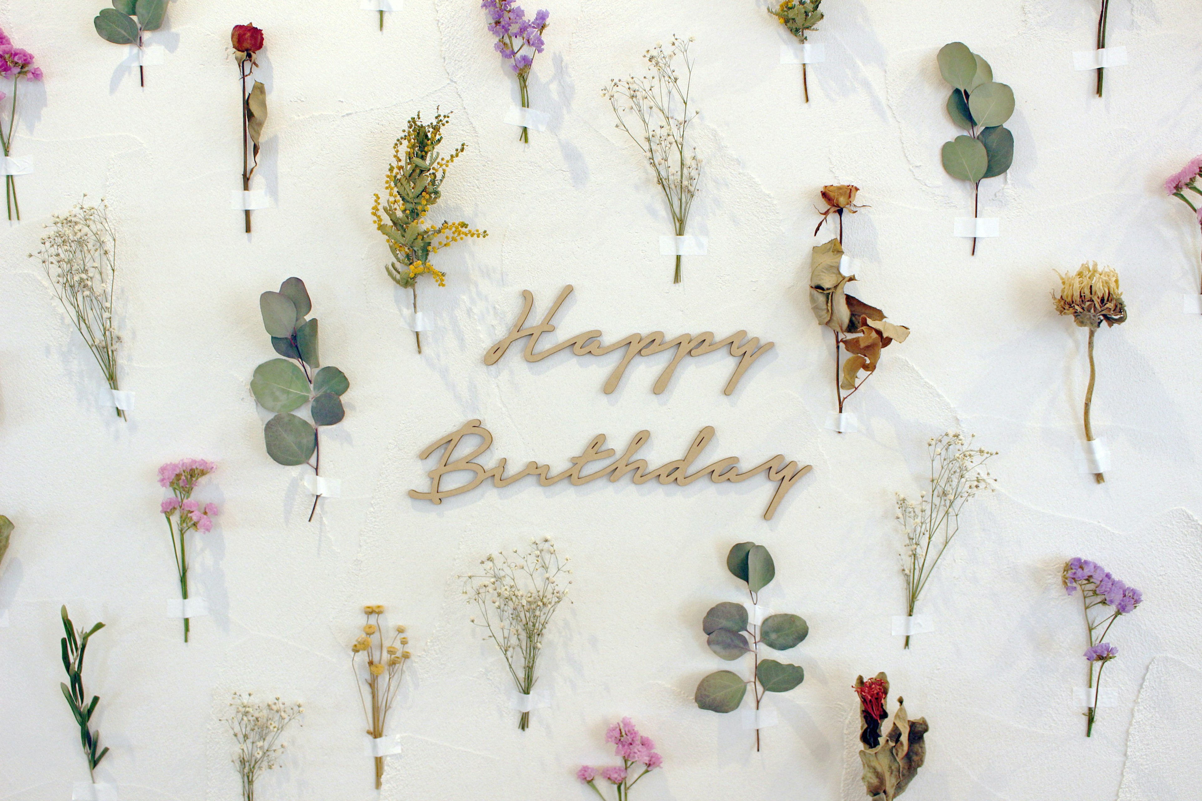 Eine Wand dekoriert mit getrockneten Blumen und Holzbuchstaben, die Happy Birthday sagen