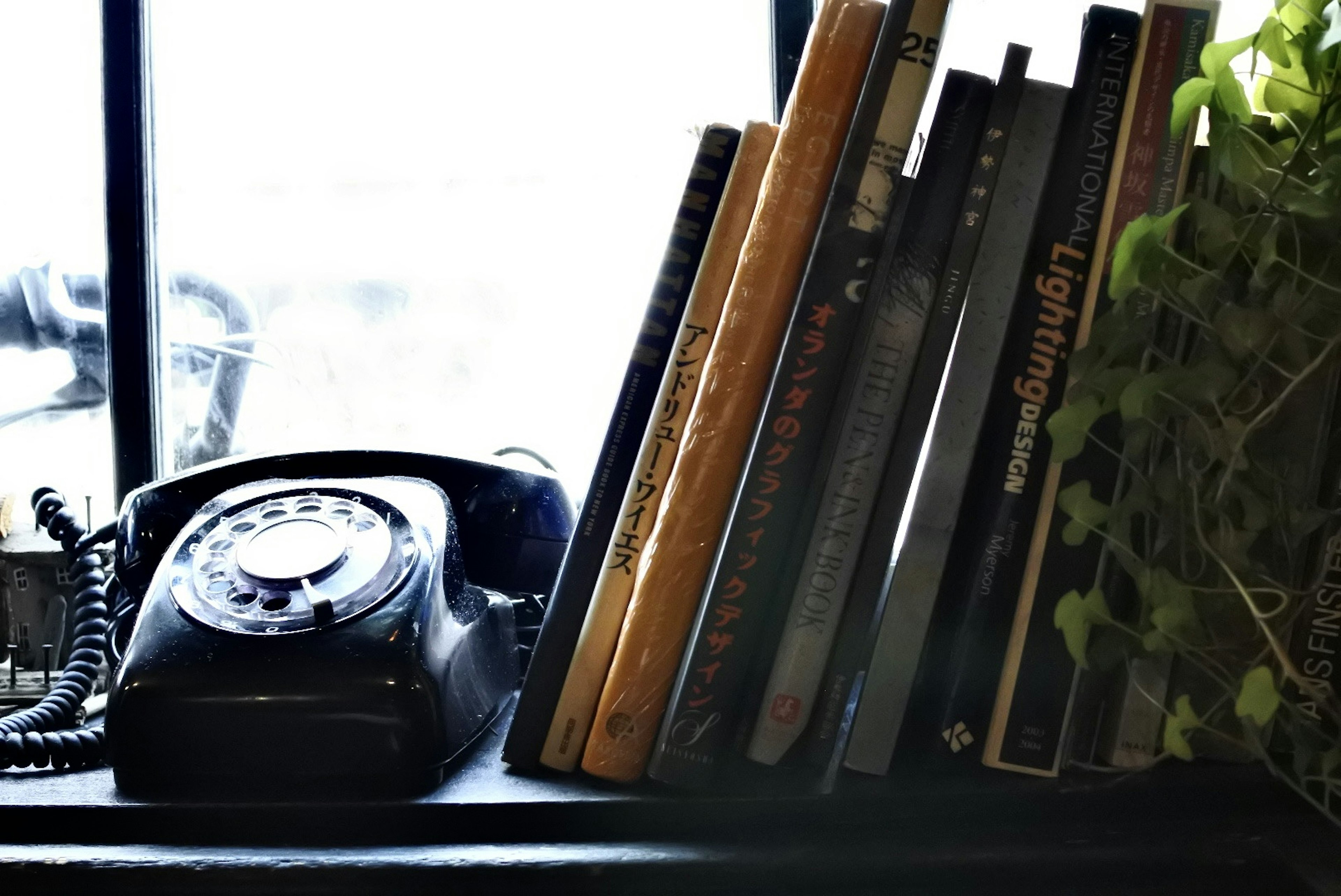 A vintage black telephone next to a stack of books on a windowsill