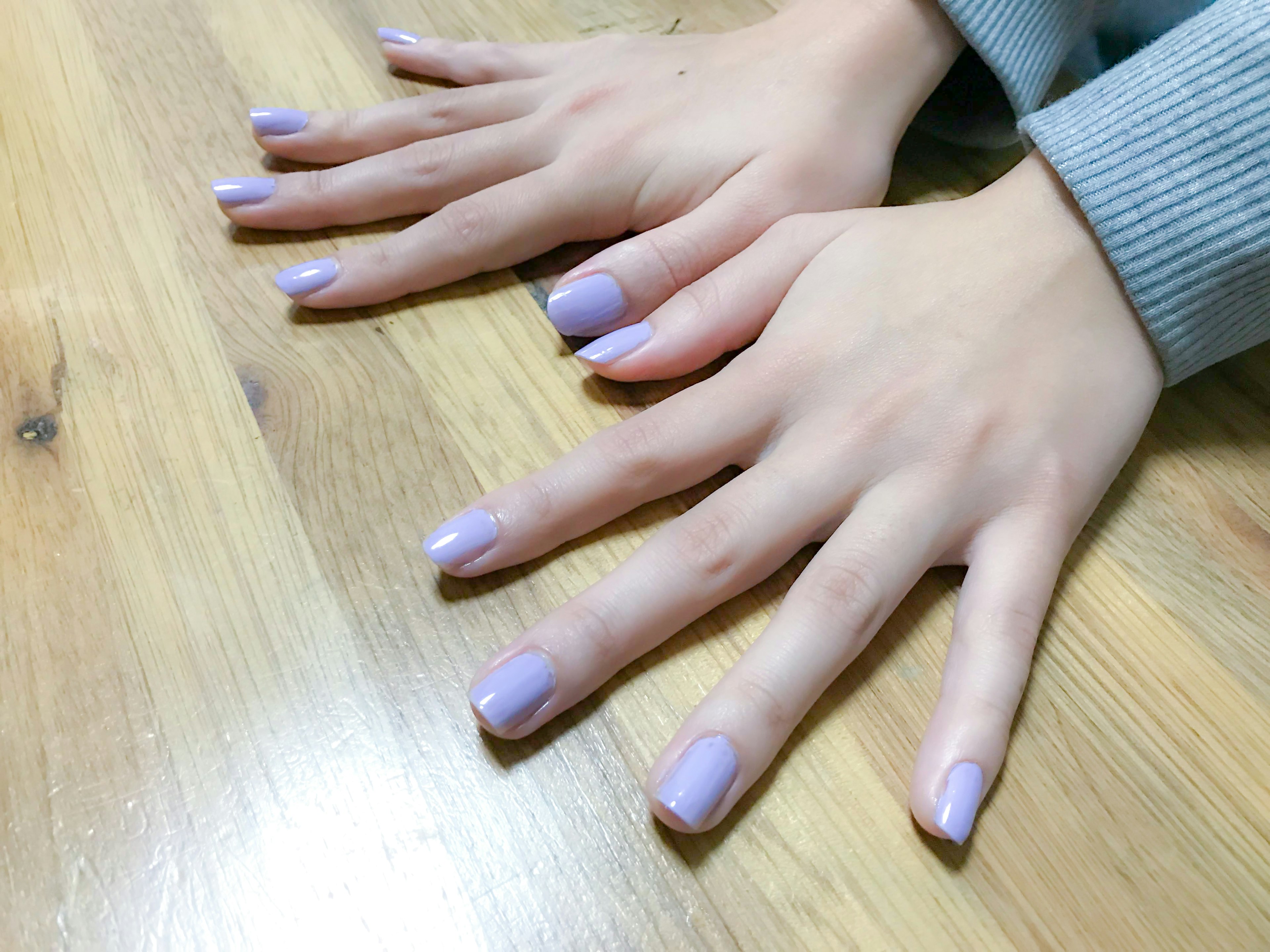 Hands with lavender nail polish resting on a wooden surface