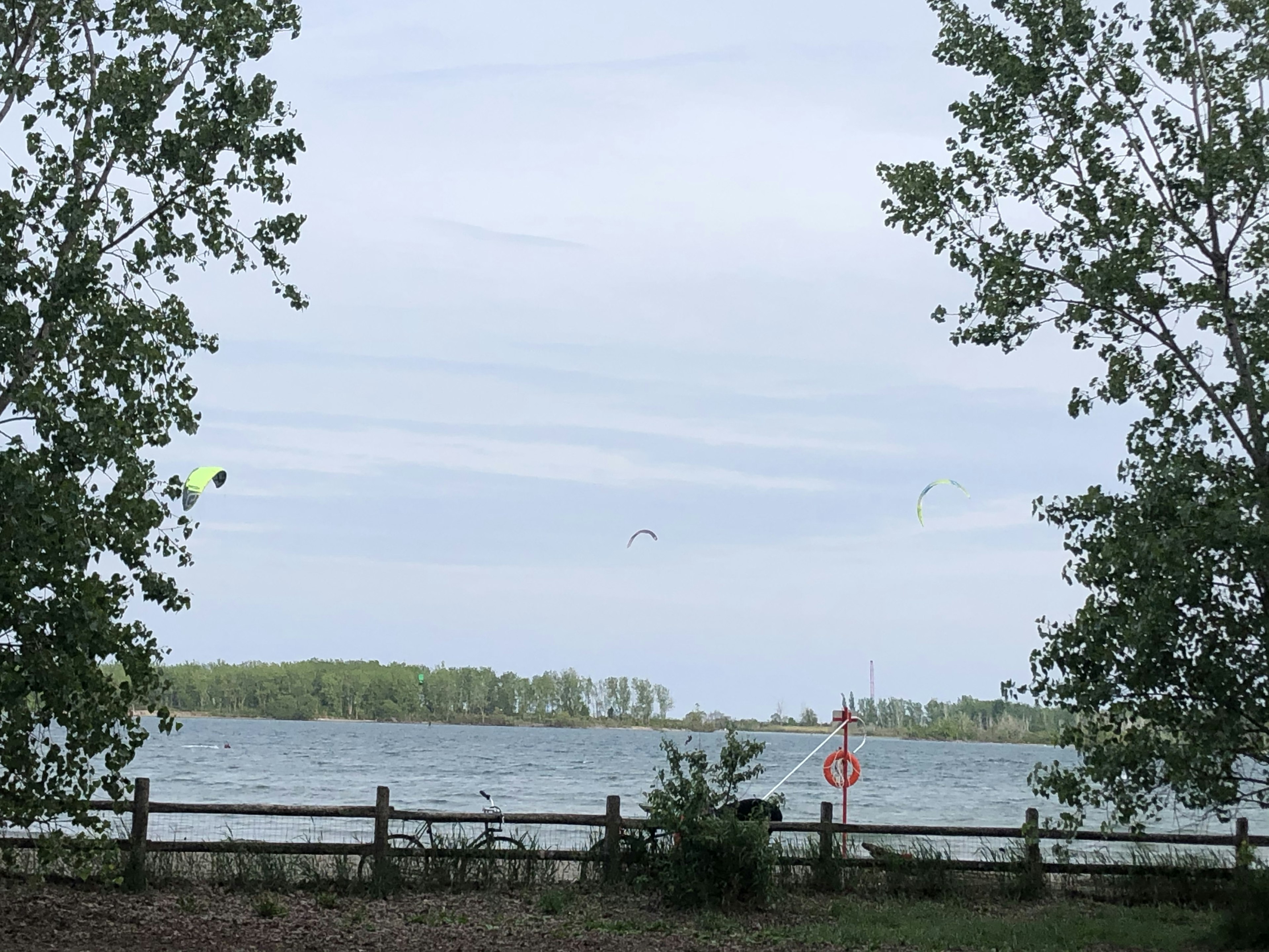 Landschaft eines Sees mit Bäumen und Menschen beim Kitesurfen