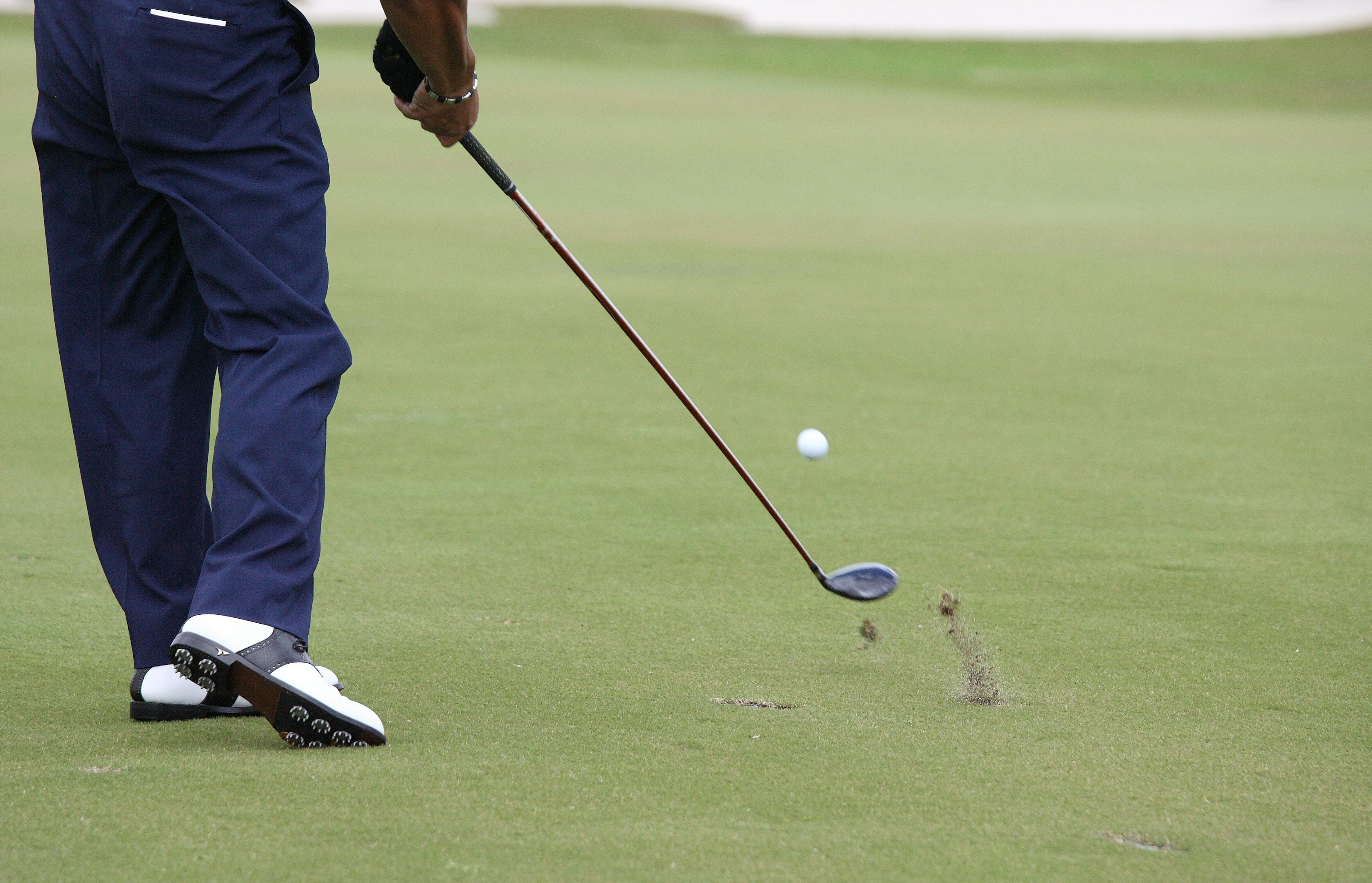 A man's hand holding a golf club with a ball on the grass