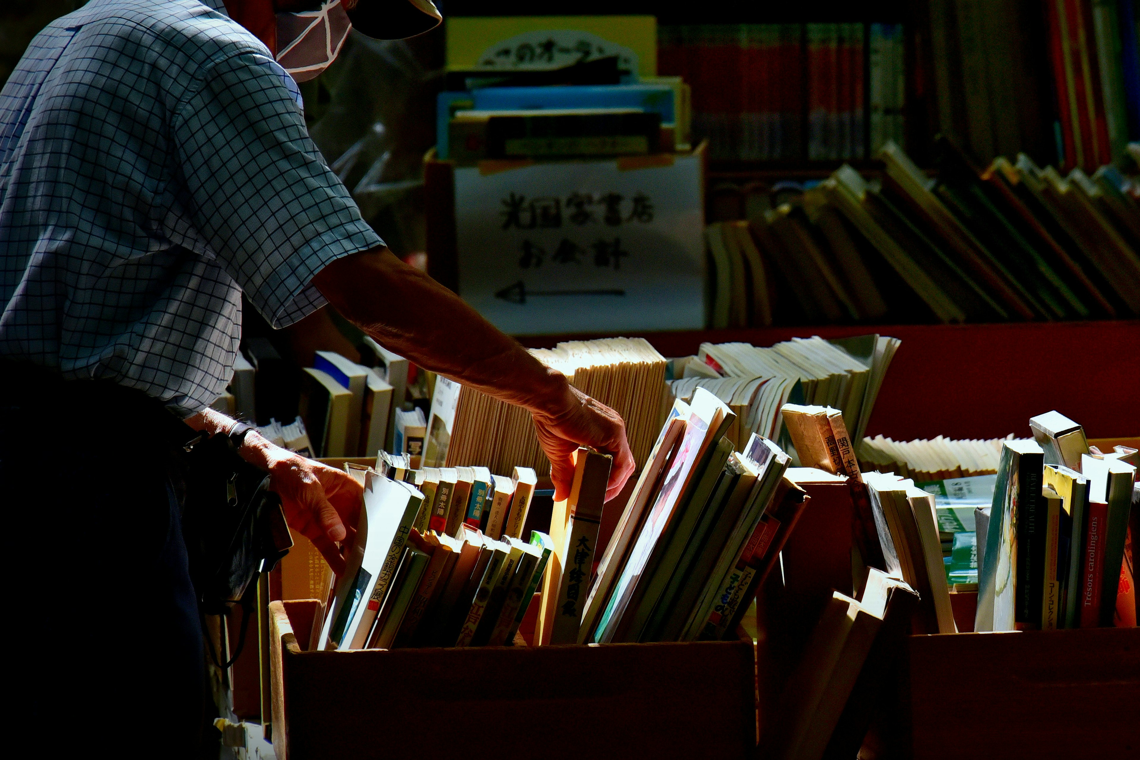 A man searching through a pile of books with bright spines in a dimly lit background