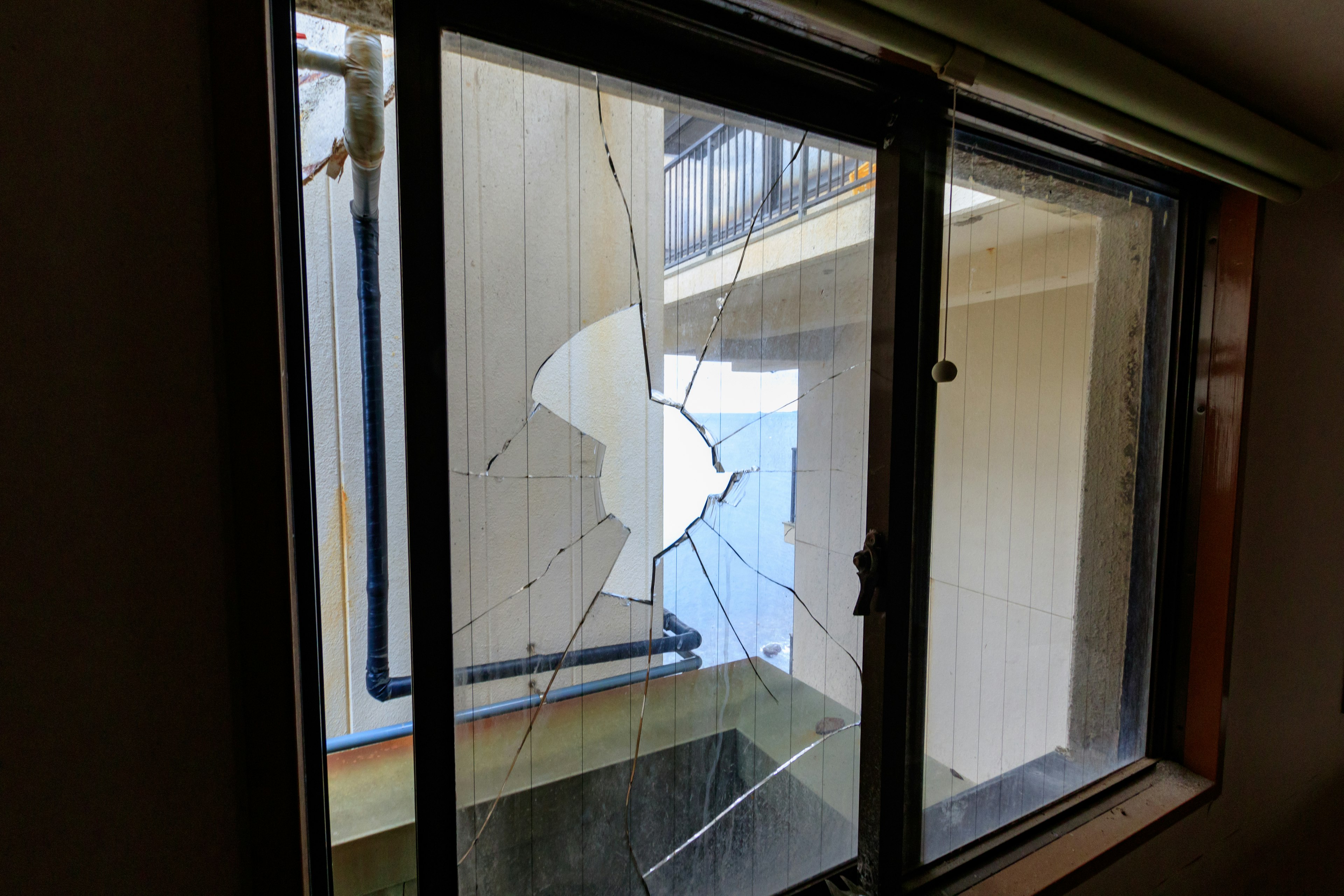 View through a broken window showing shattered glass and an exterior wall