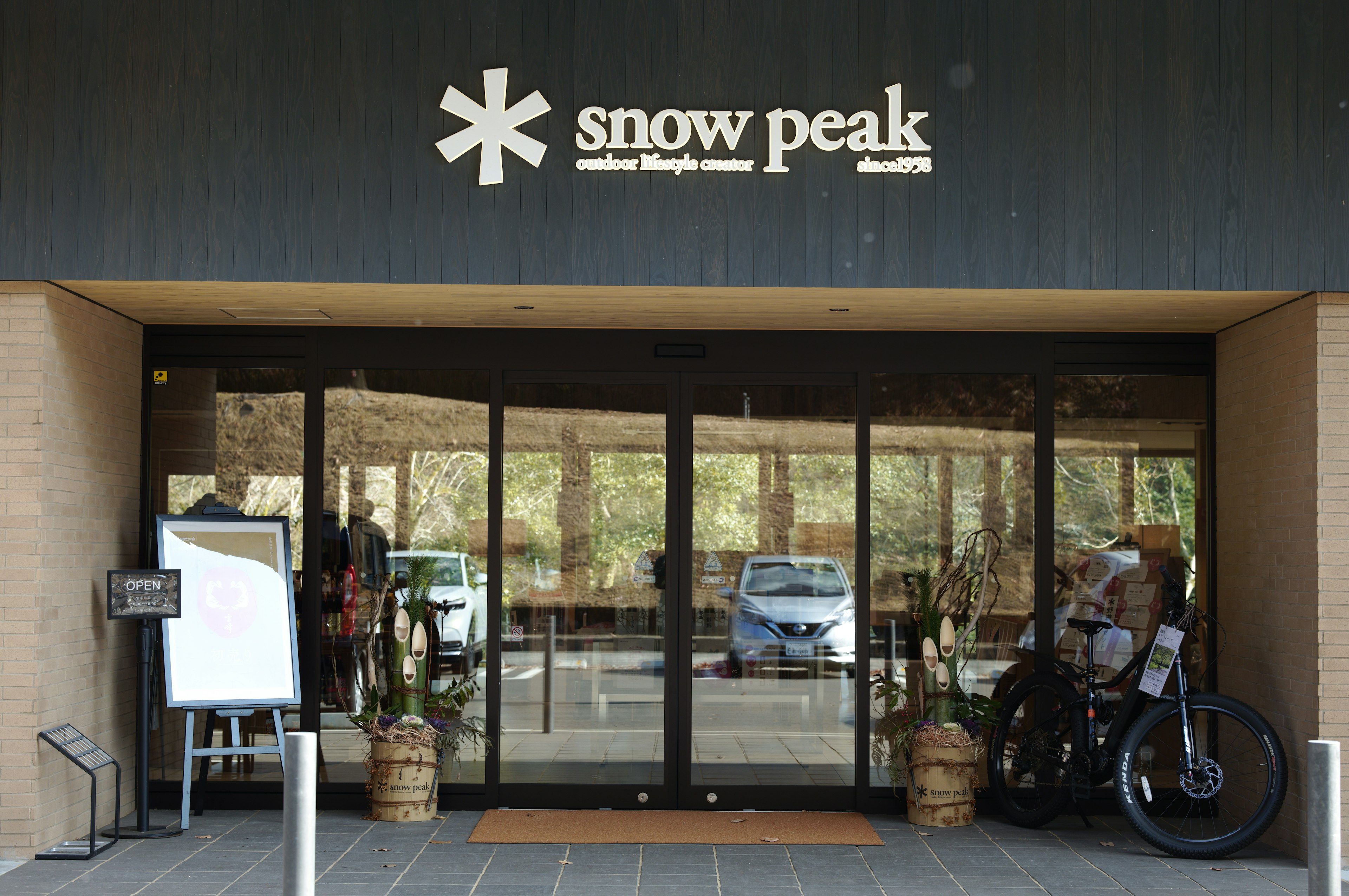 Tampilan luar pintu masuk toko Snow Peak dengan sepeda dan papan