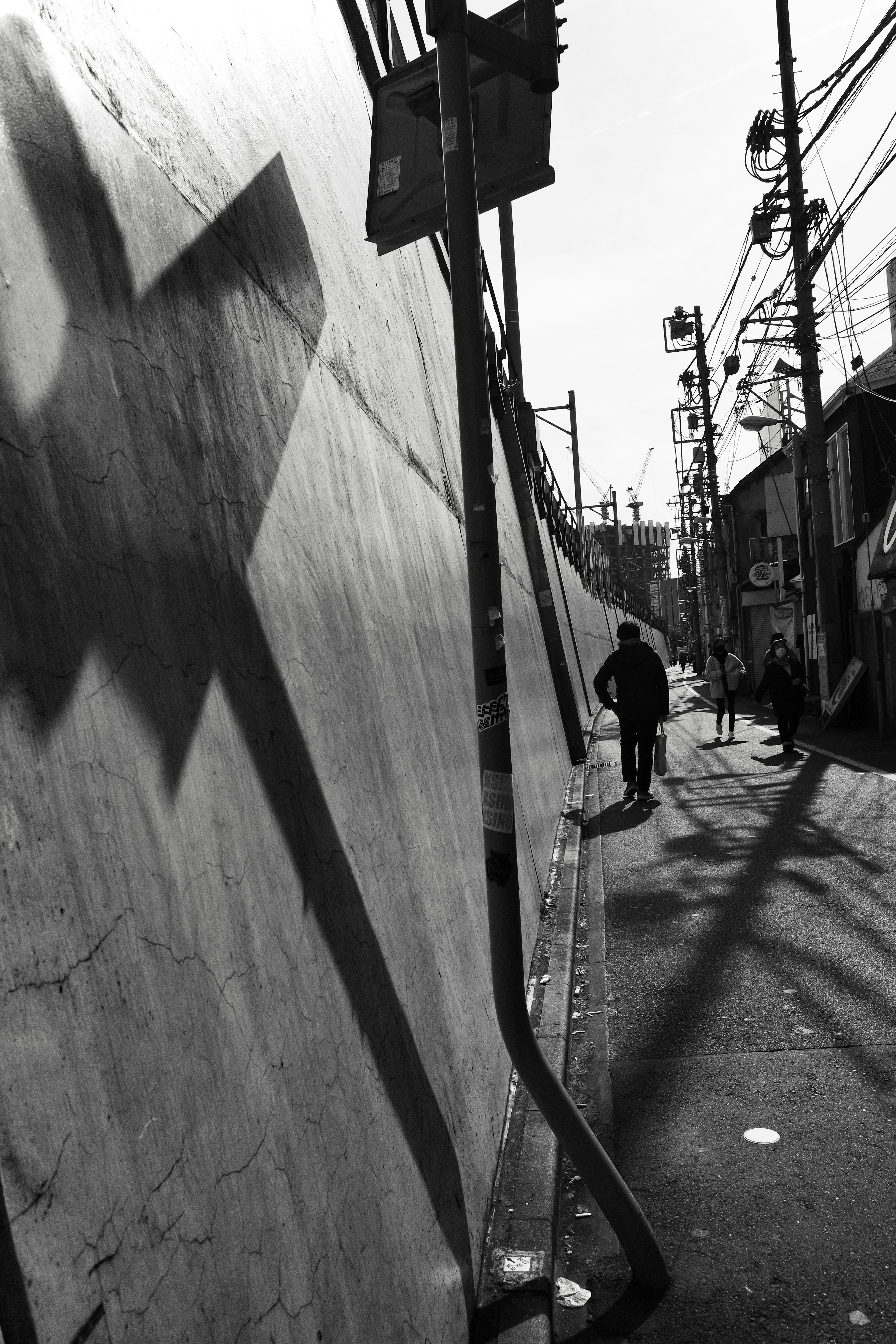 Persona caminando por una acera sombría en una escena urbana en blanco y negro