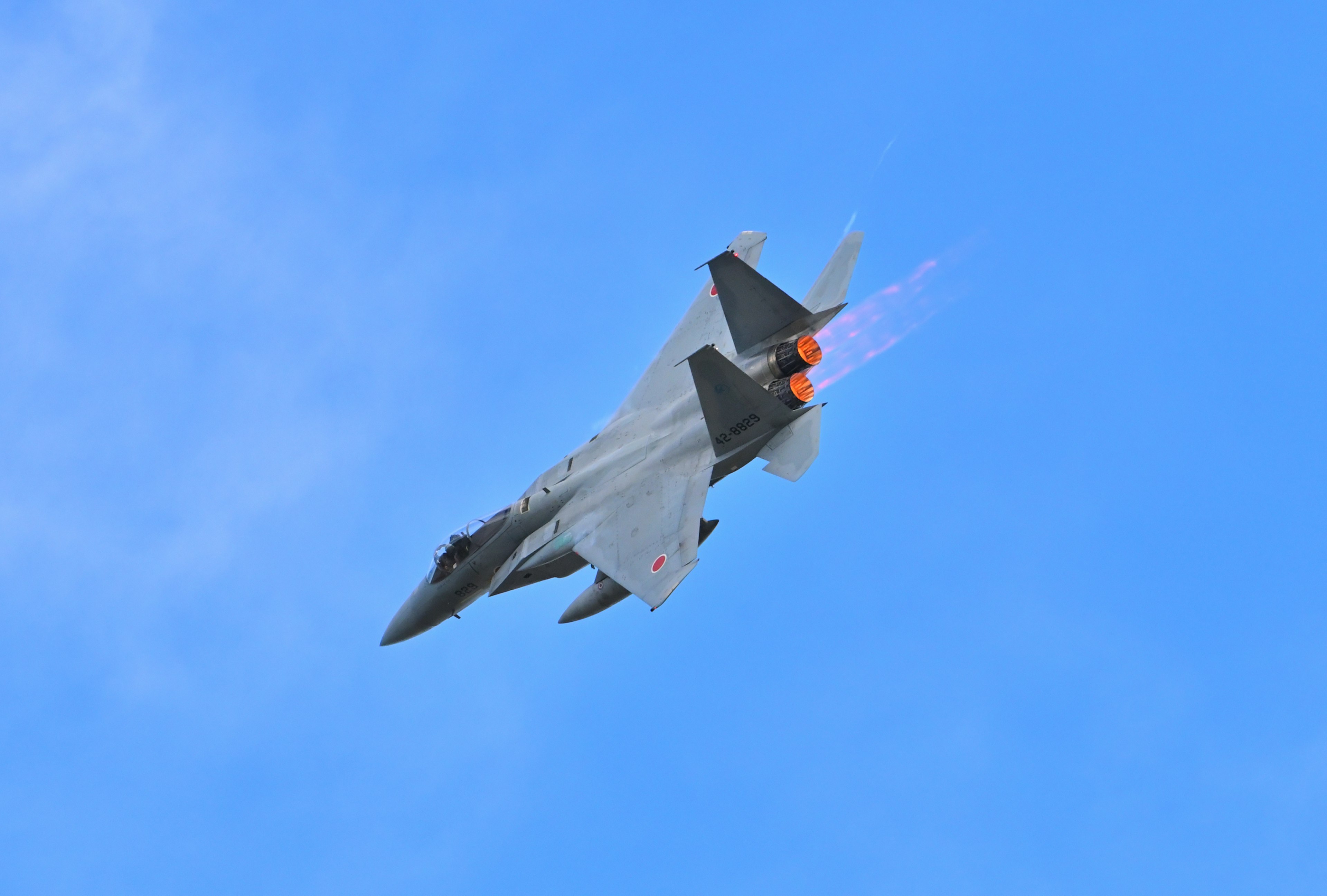 Fighter jet flying in blue sky with orange flames trailing from the rear