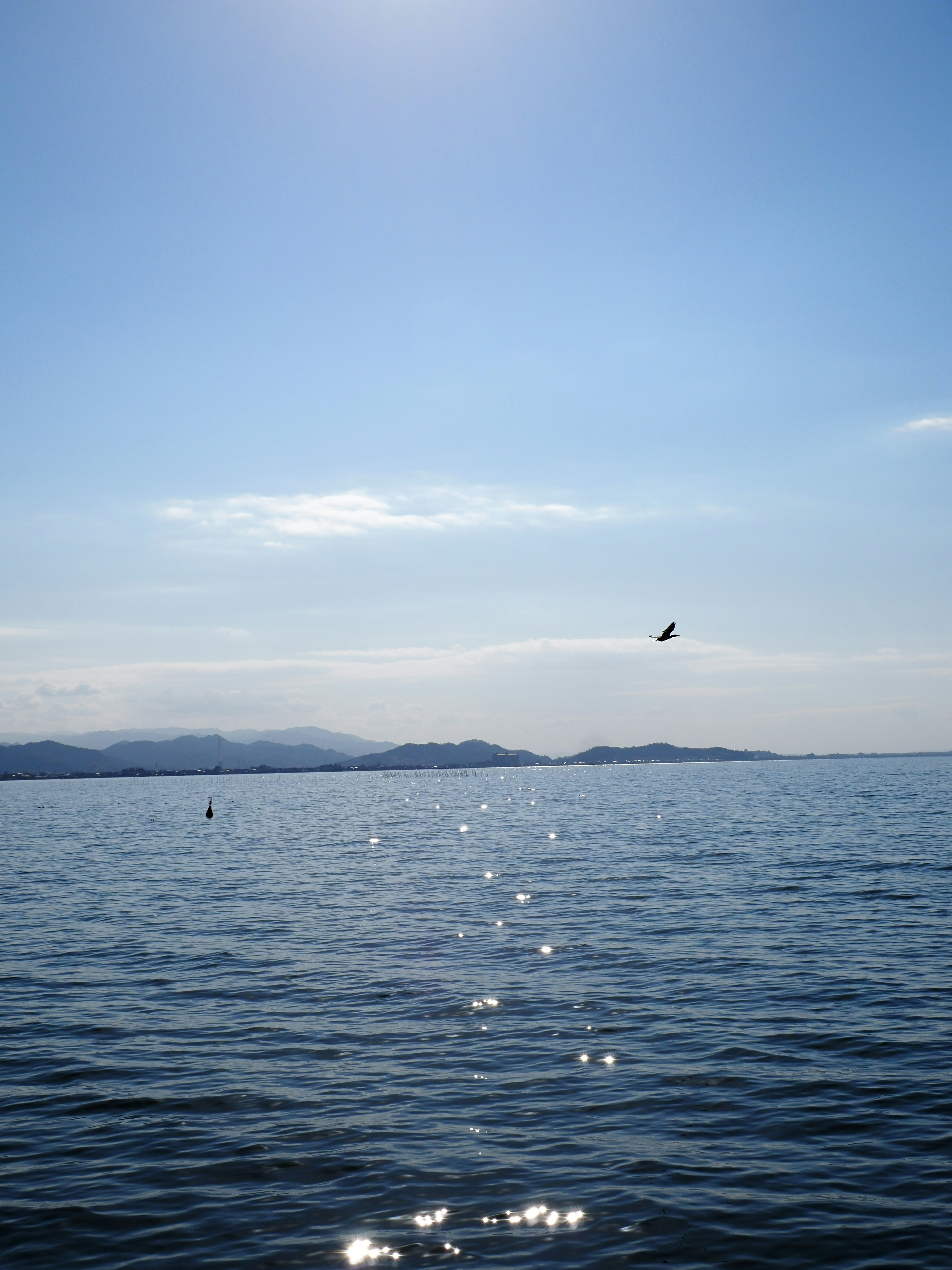 A serene view of blue sea and sky with sparkling water surface and distant islands