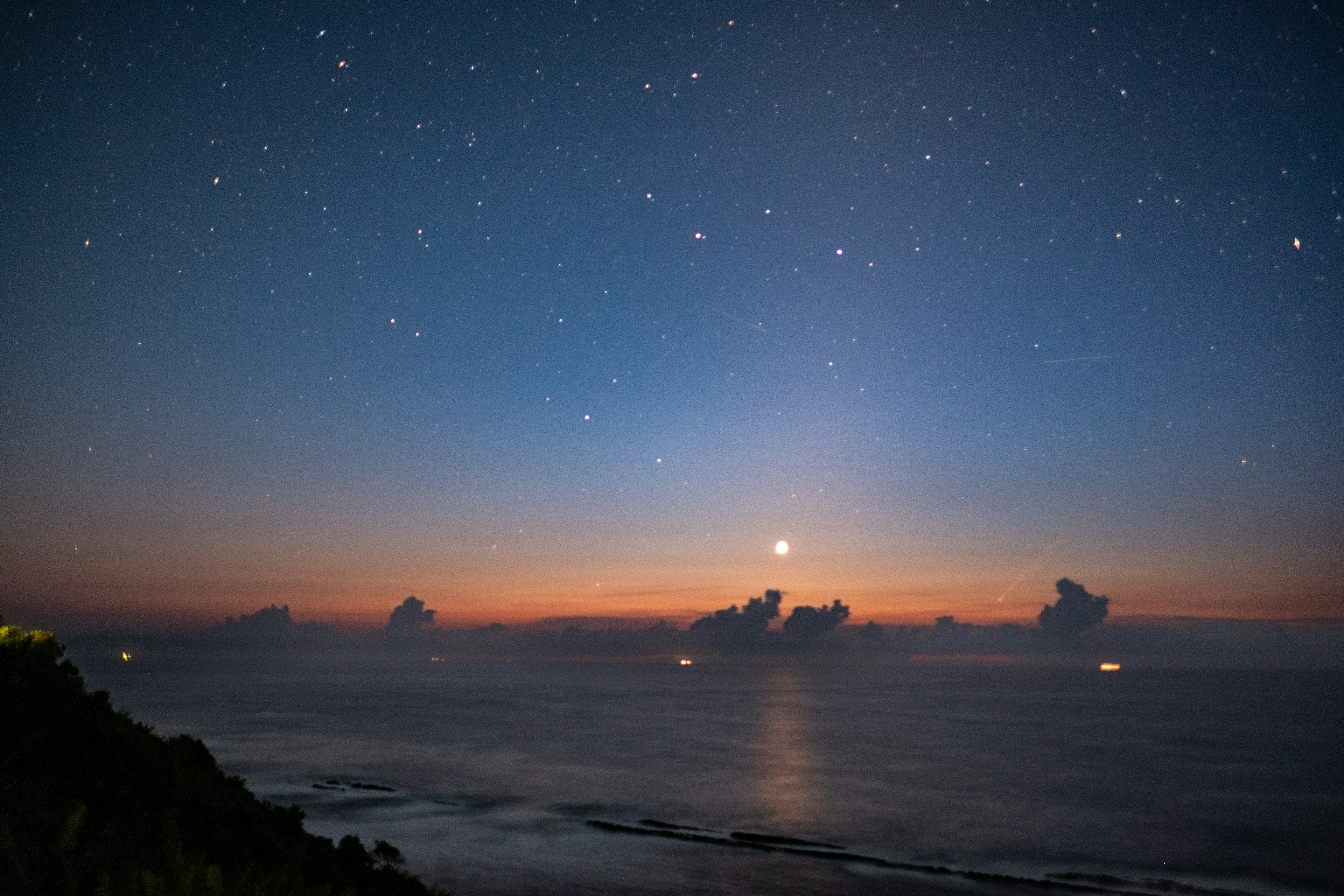 Cielo estrellado sobre el océano con un atardecer y nubes