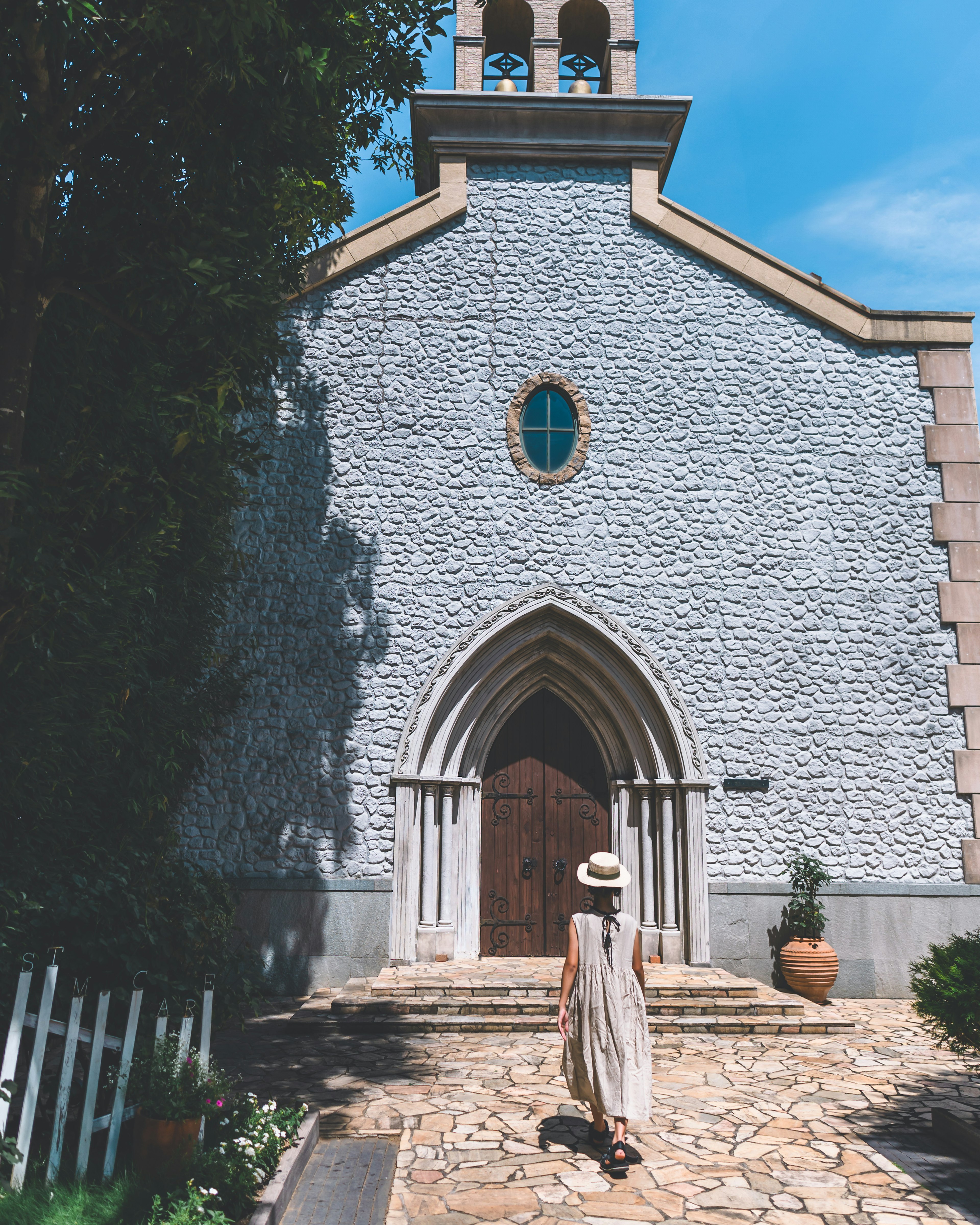 A woman walking in front of a stone church with an arched entrance