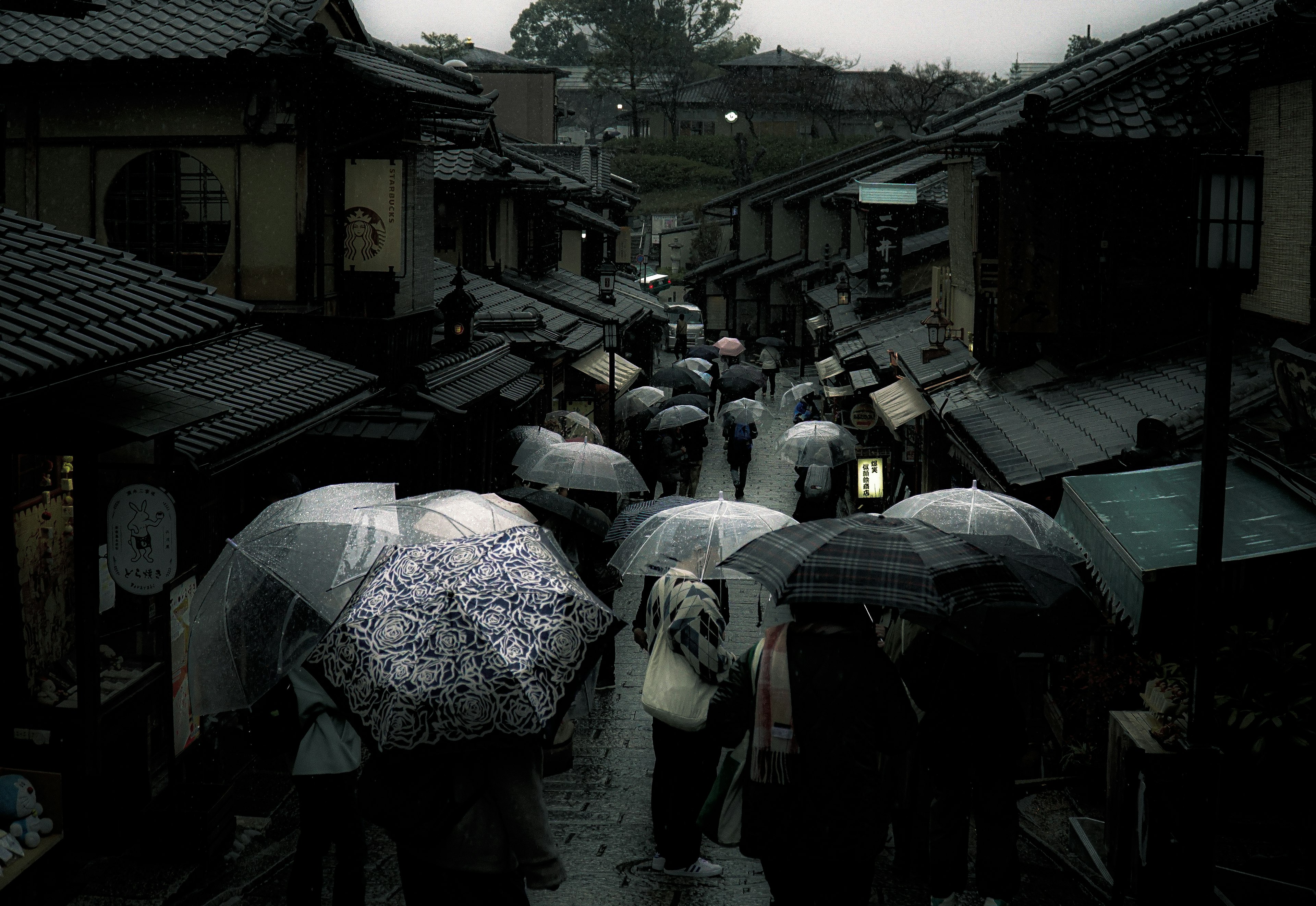 雨の中の傘を持った人々が歩く古い街並み