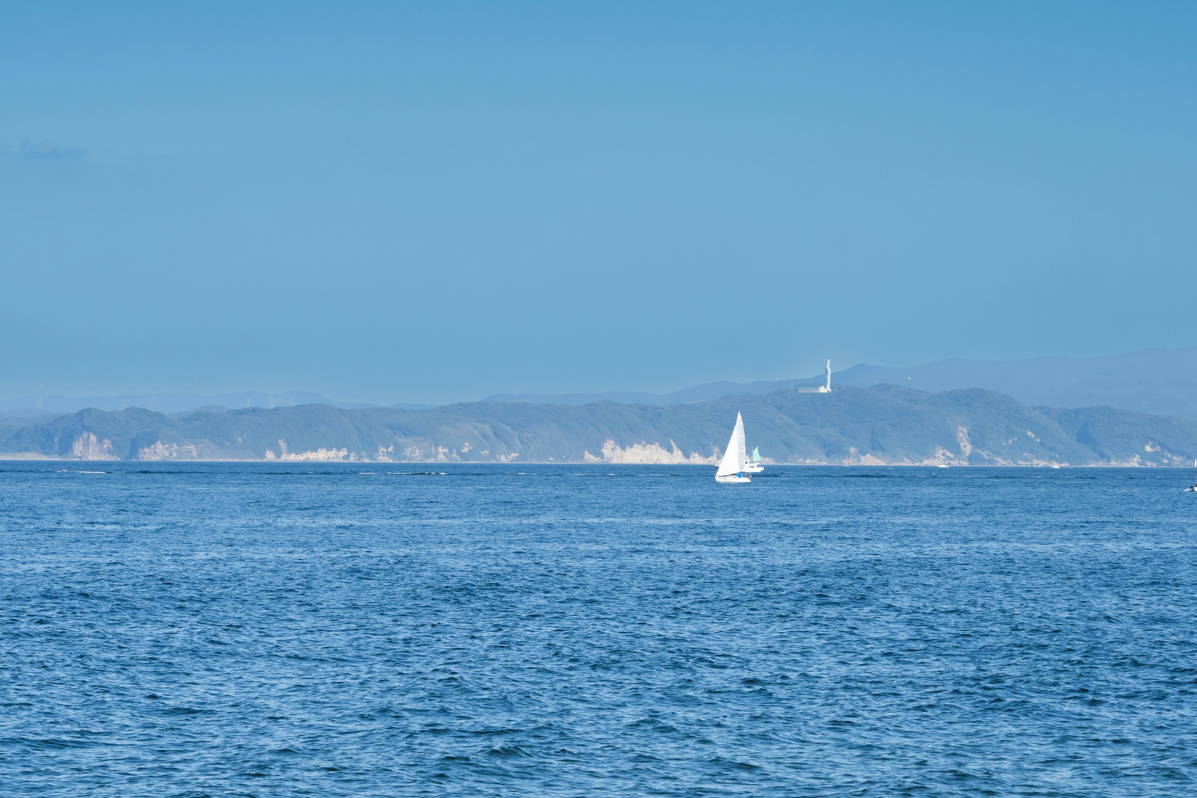 Un velero blanco en un mar azul con montañas a lo lejos