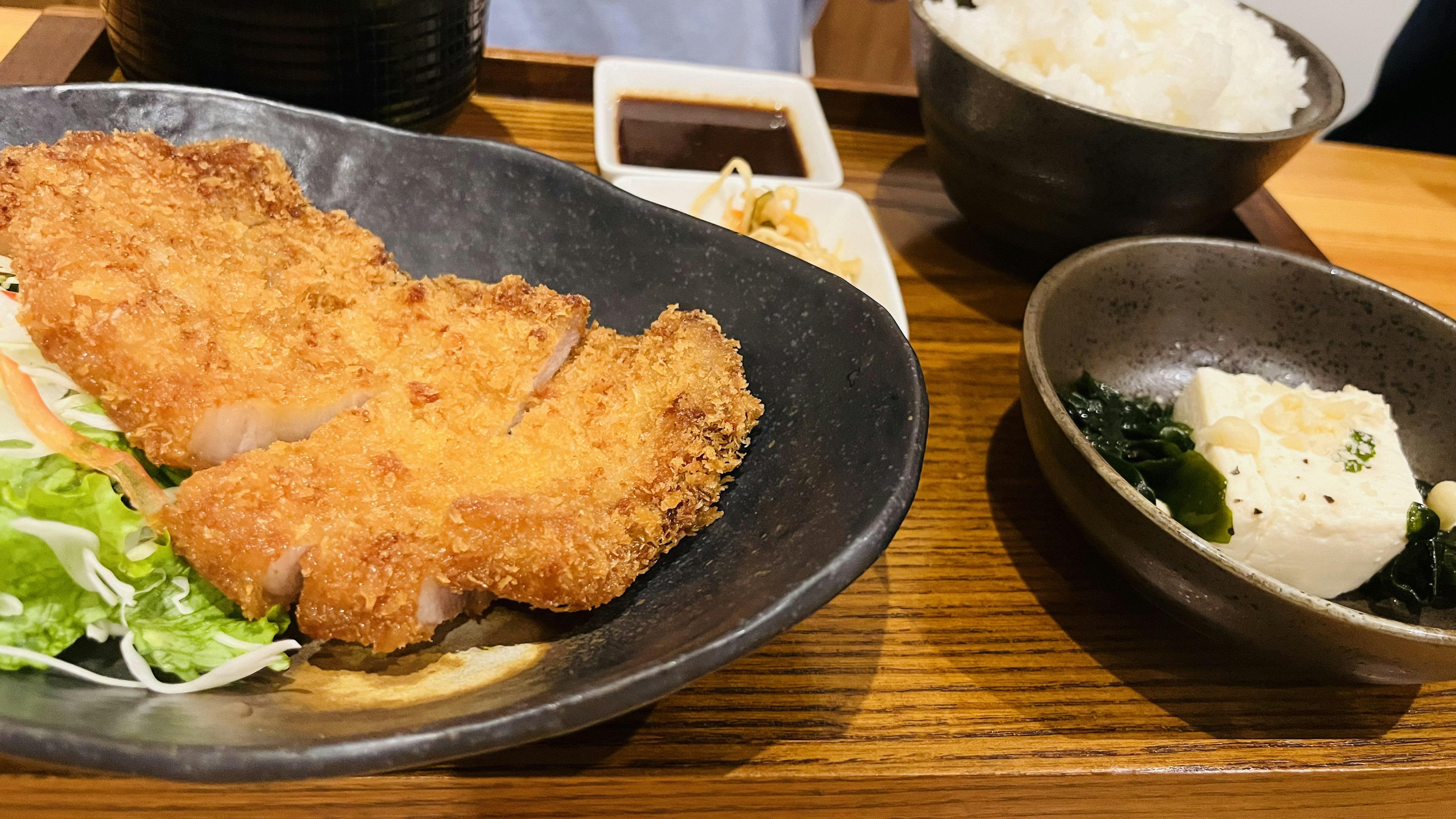 Plate of crispy fried pork with salad, served with white rice and a small side dish