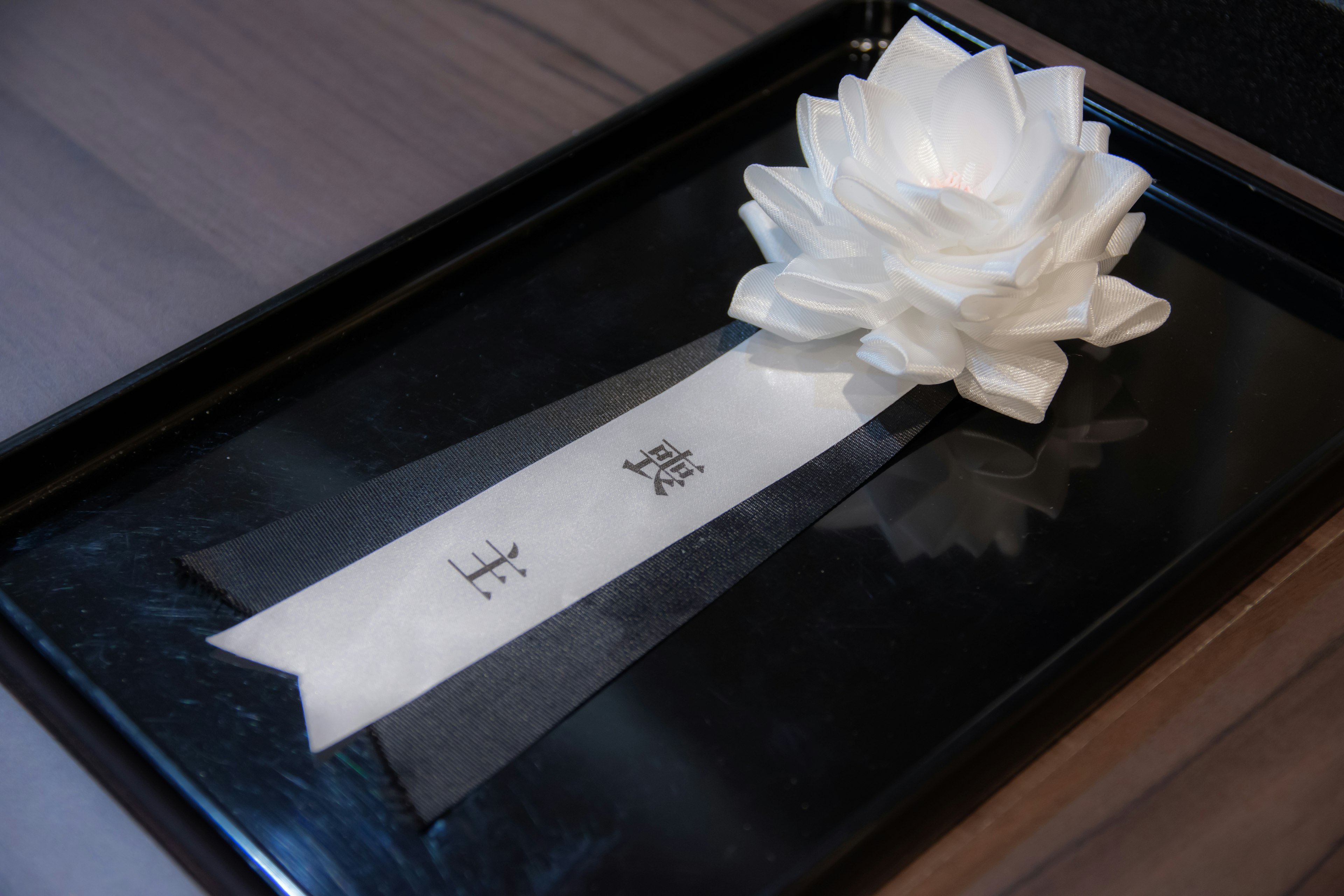 A white flower decoration with ribbons placed on a black tray