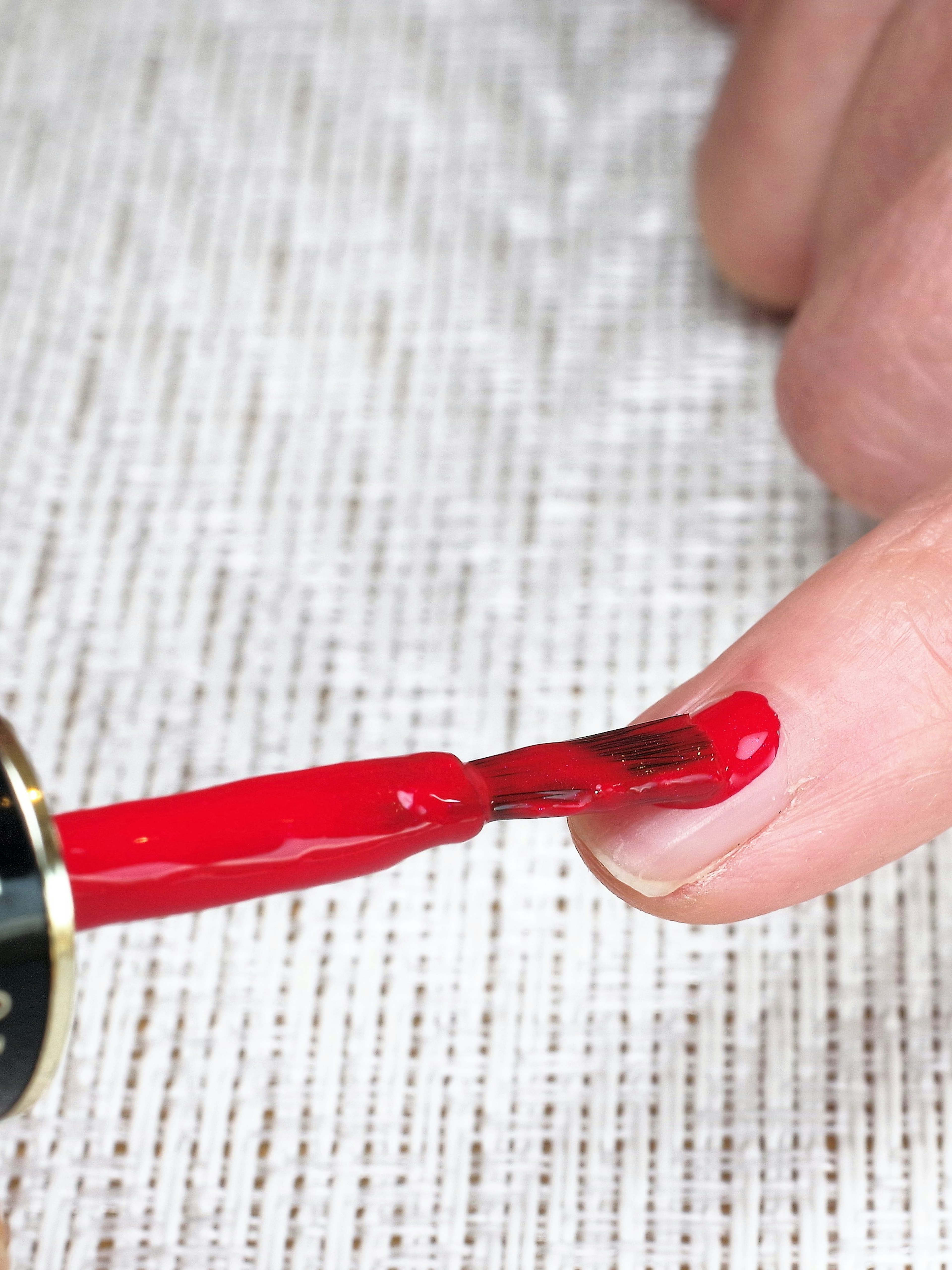 Primer plano de un dedo aplicando esmalte de uñas rojo