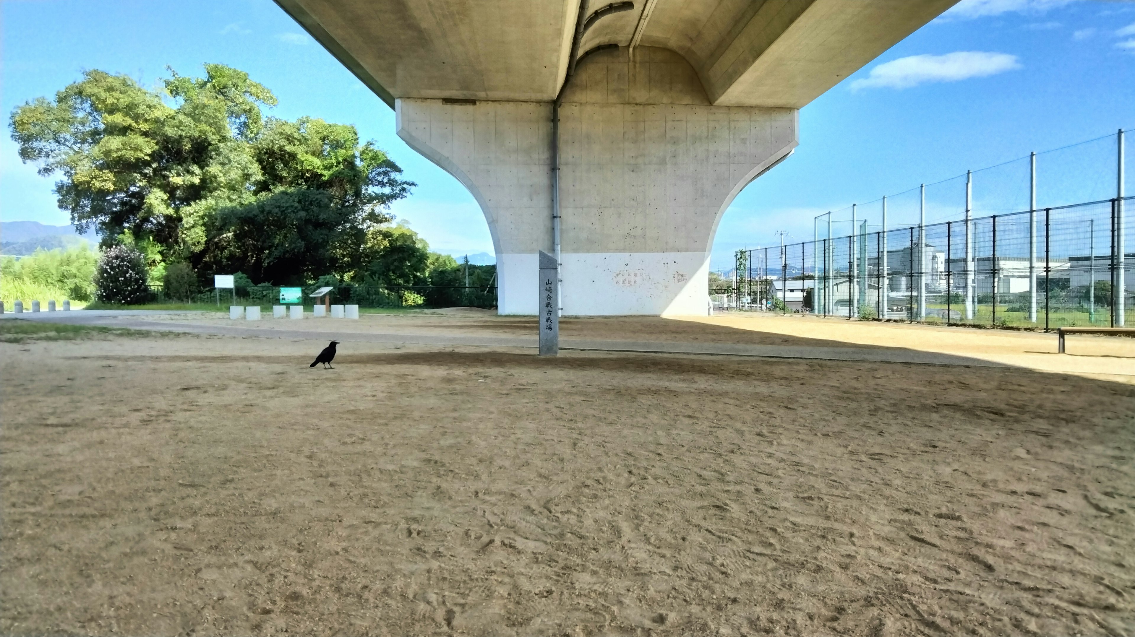 Ein sandiger Bereich unter einer Brücke mit blauem Himmel und Bäumen im Hintergrund