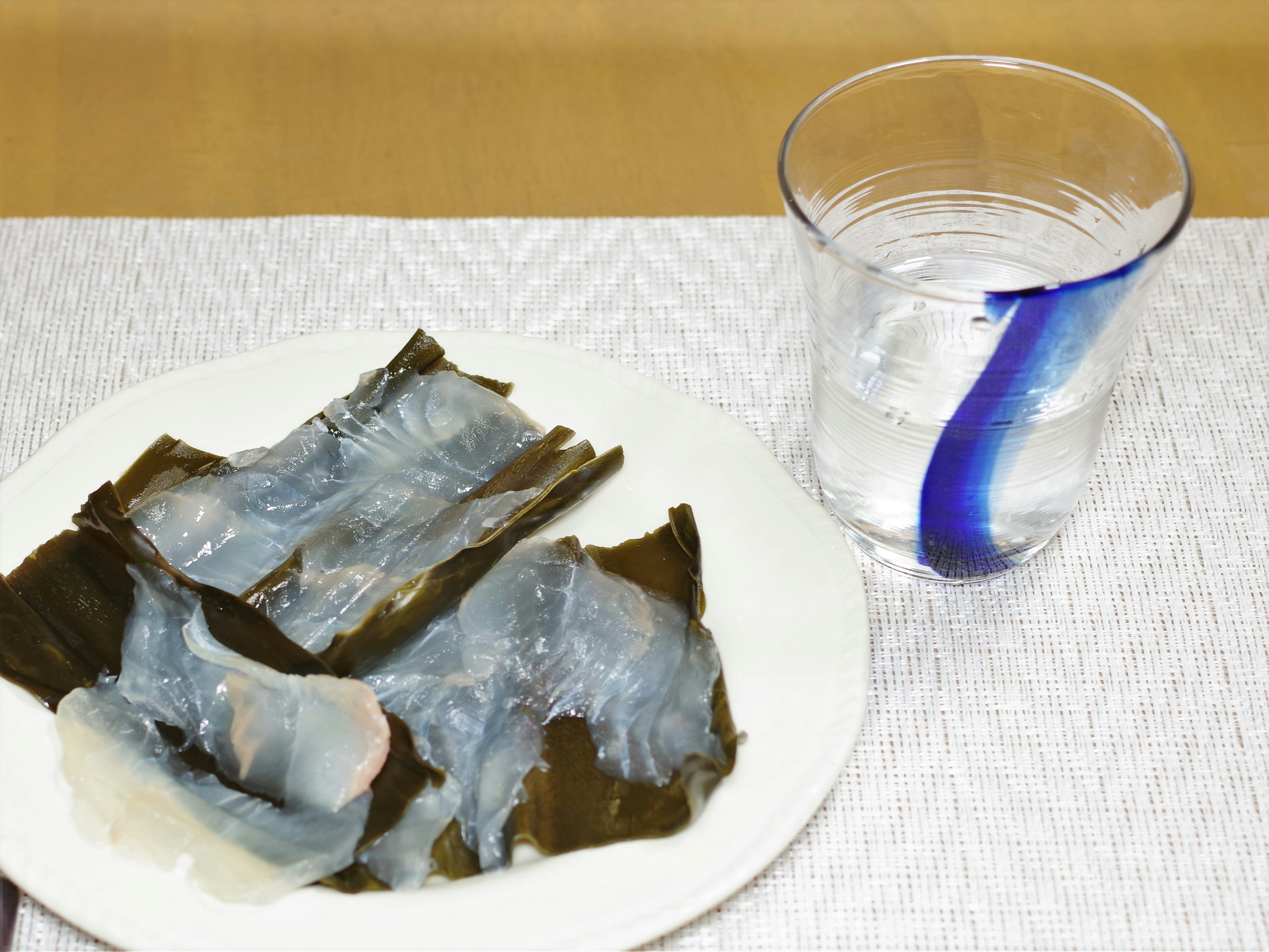 Ein Teller mit Algen und durchsichtigen Meeresfrüchten sowie ein Glas Wasser