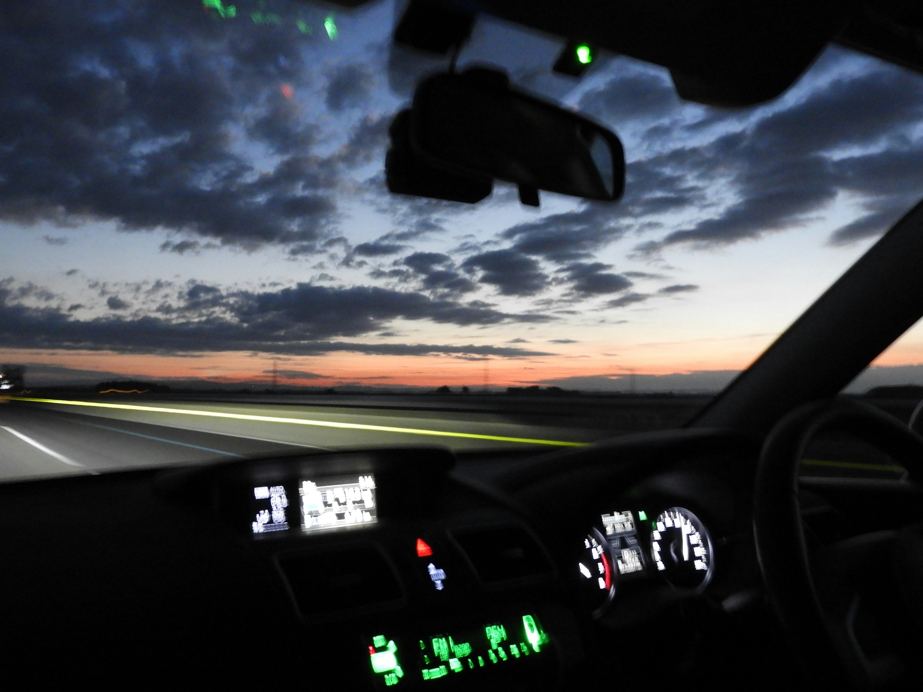 Vista interior de un coche conduciendo por una carretera al amanecer con display del tablero y navegación