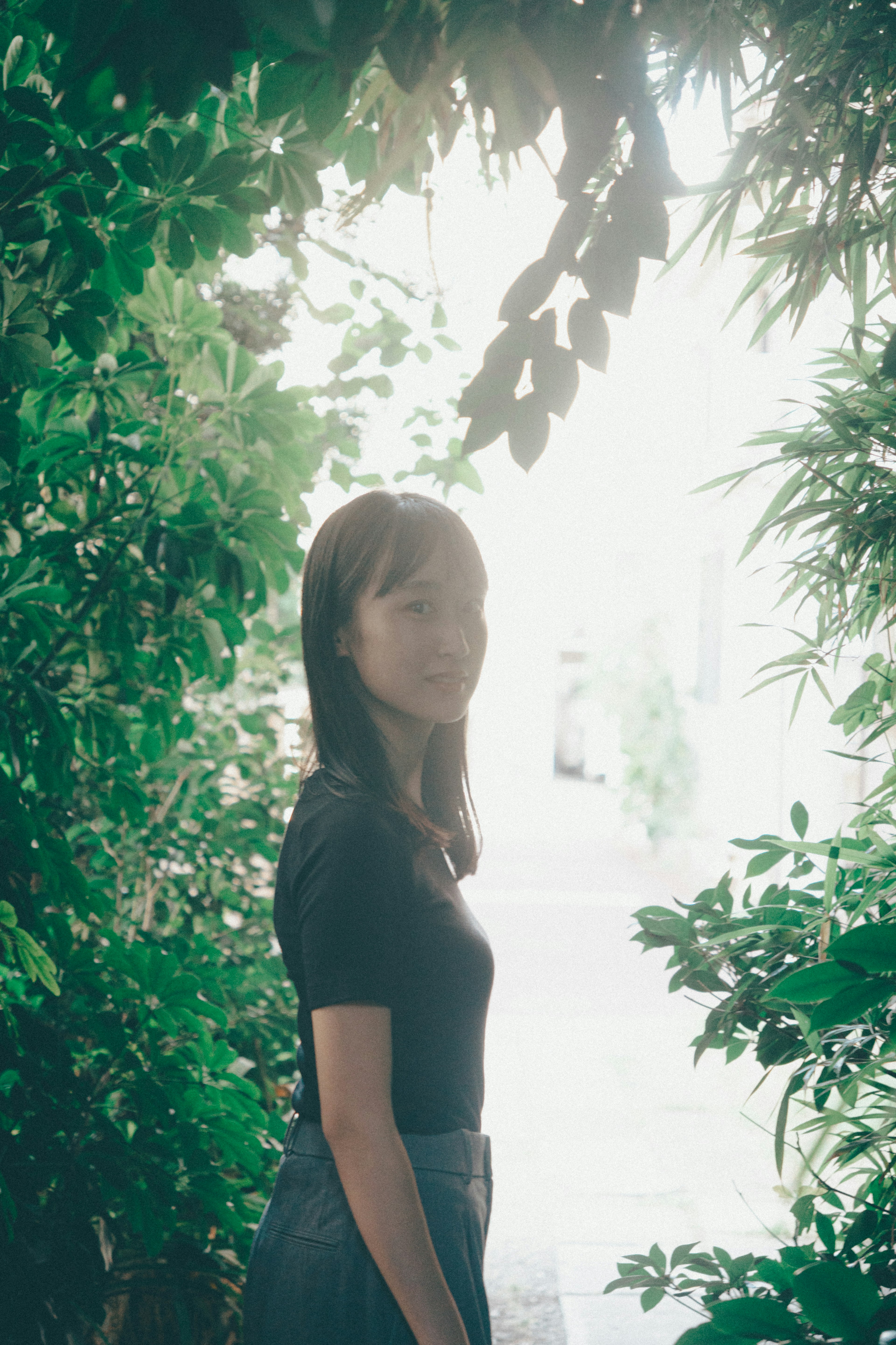 Una mujer de pie entre plantas verdes con luz suave al fondo