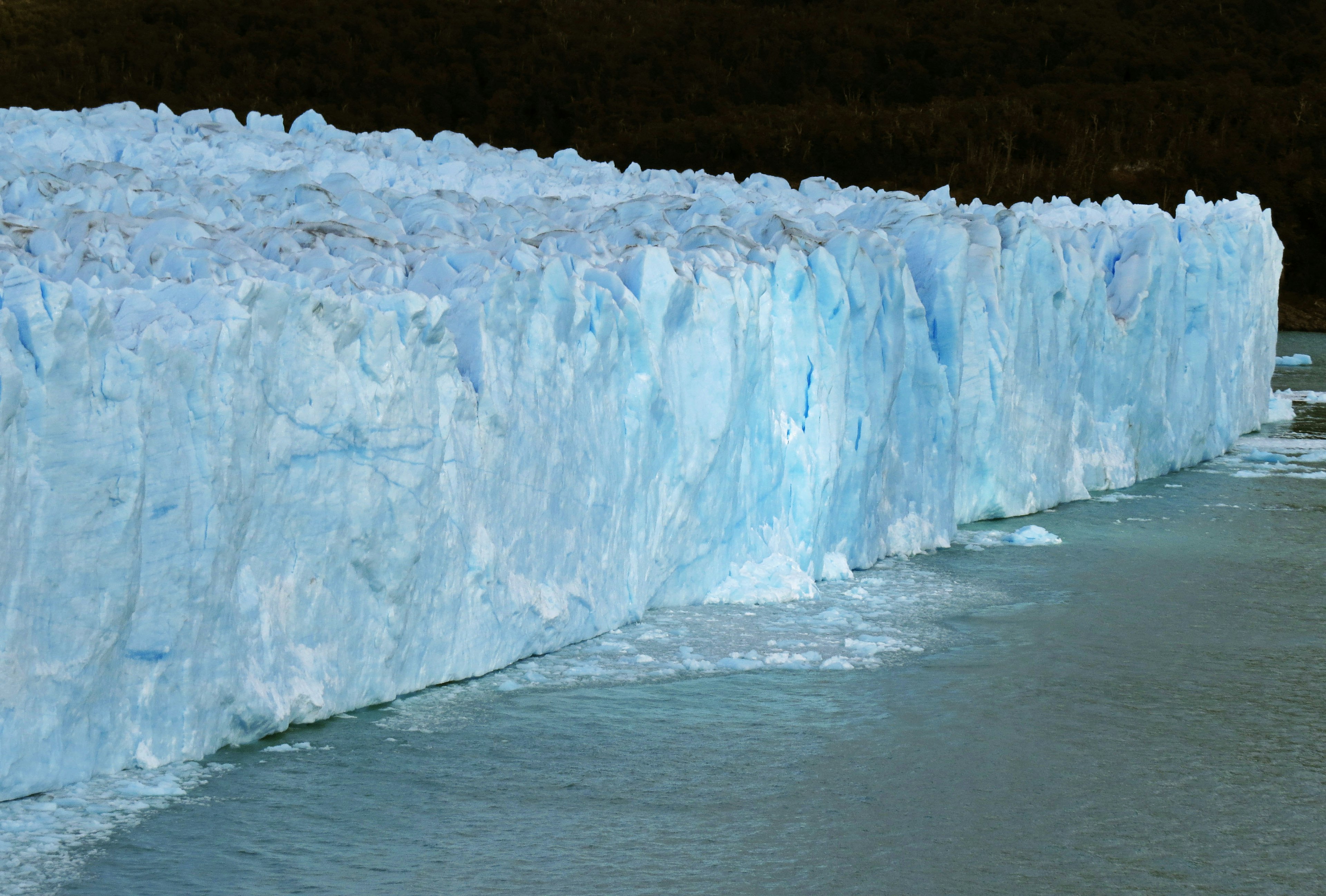 Muro di ghiaccio blu di un ghiacciaio con riflessi nell'acqua