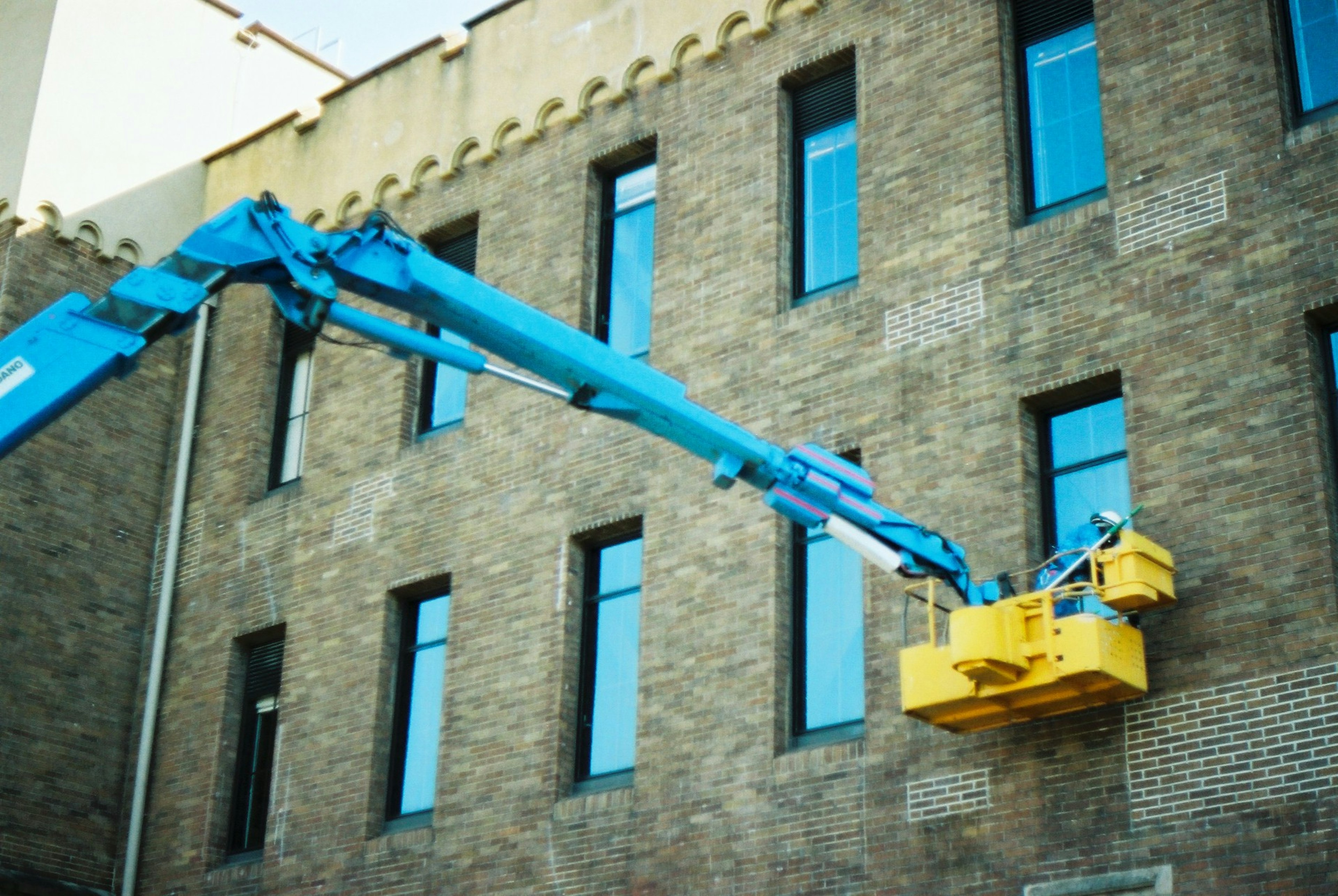 Ouvrier sur un élévateur jaune fixé à un mur de bâtiment bras bleu s'étendant