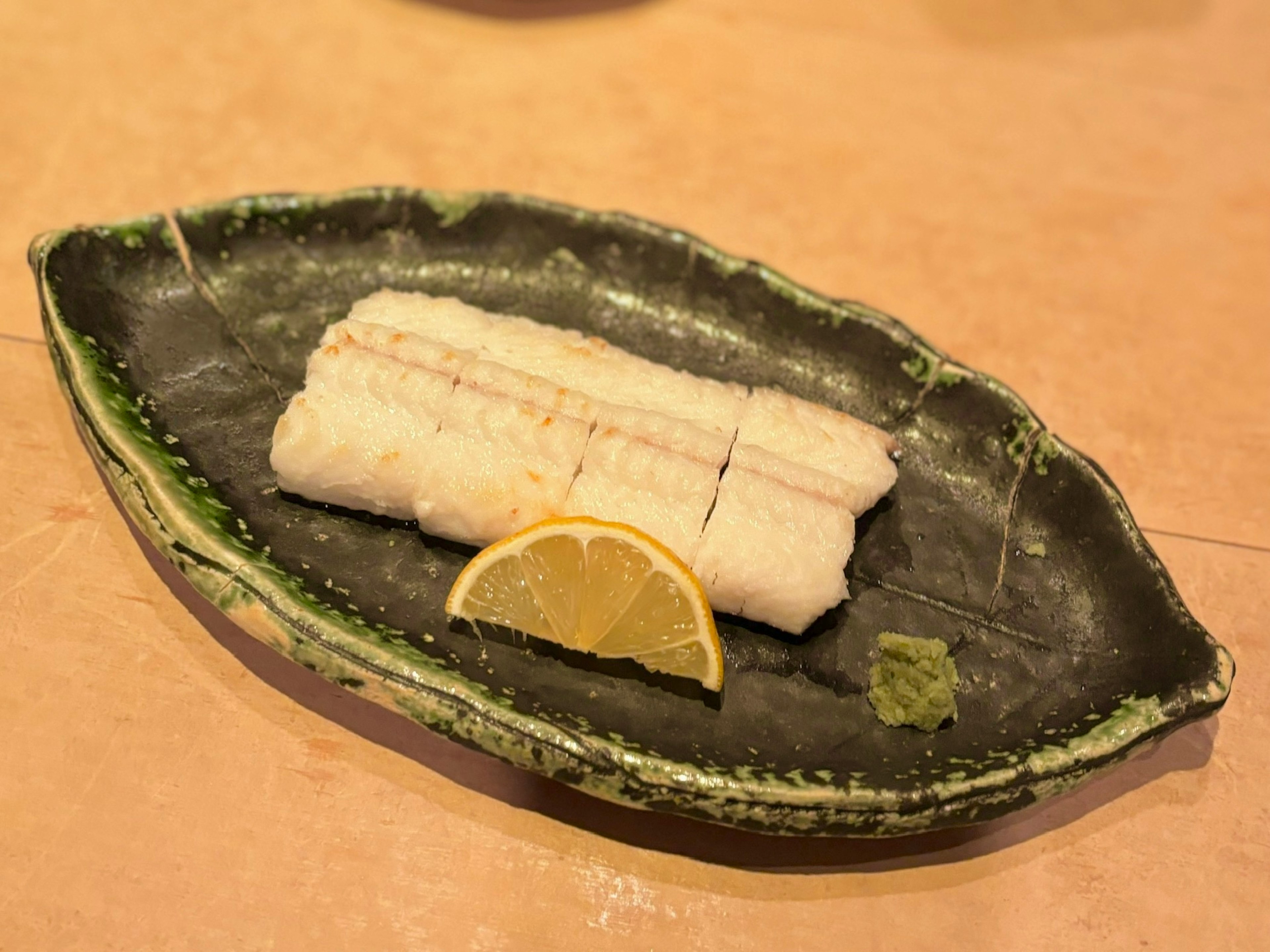 Sliced white fish sashimi on a green plate with lemon and wasabi