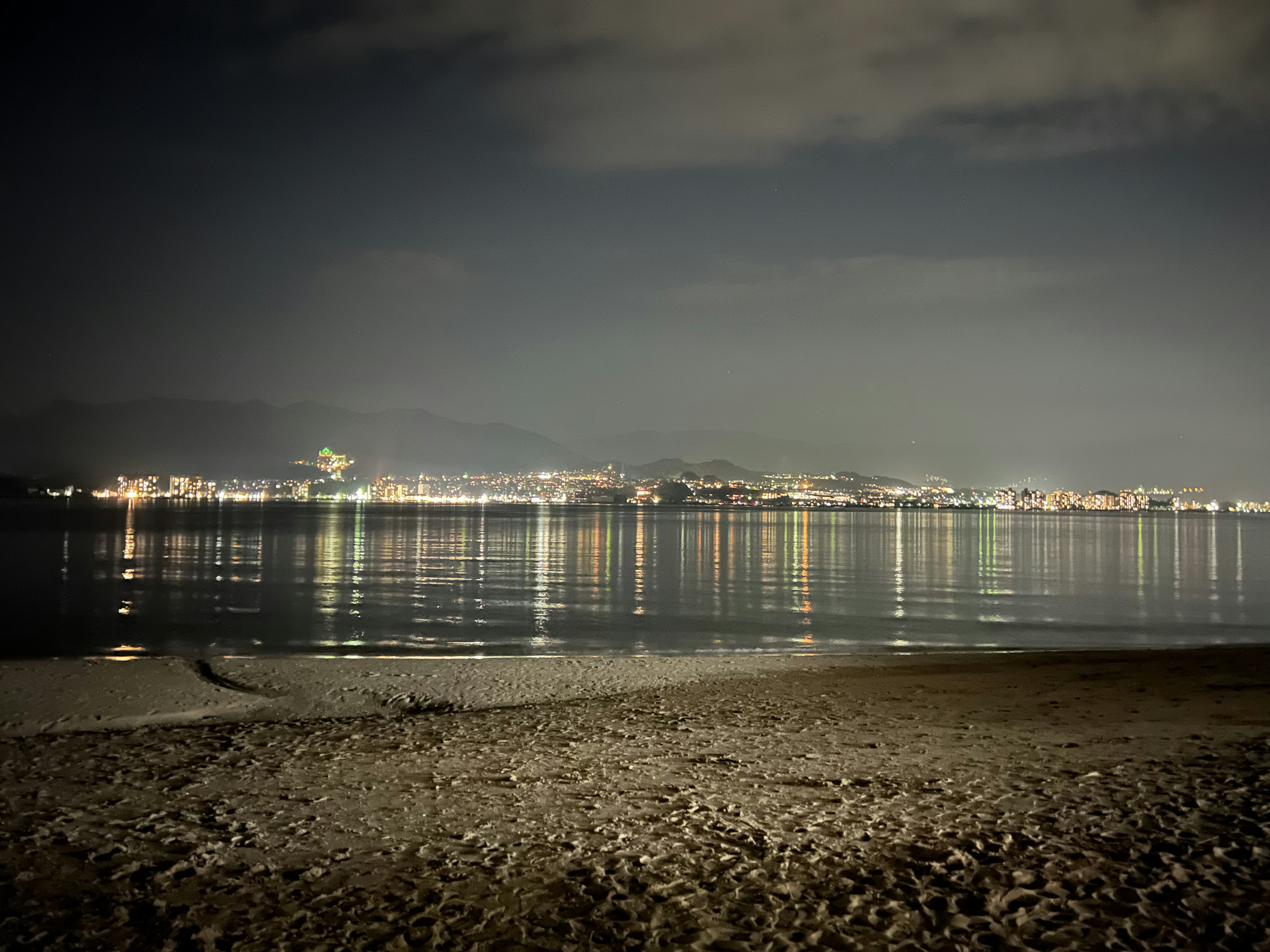 Nighttime beach scene with reflections of lights and calm waves