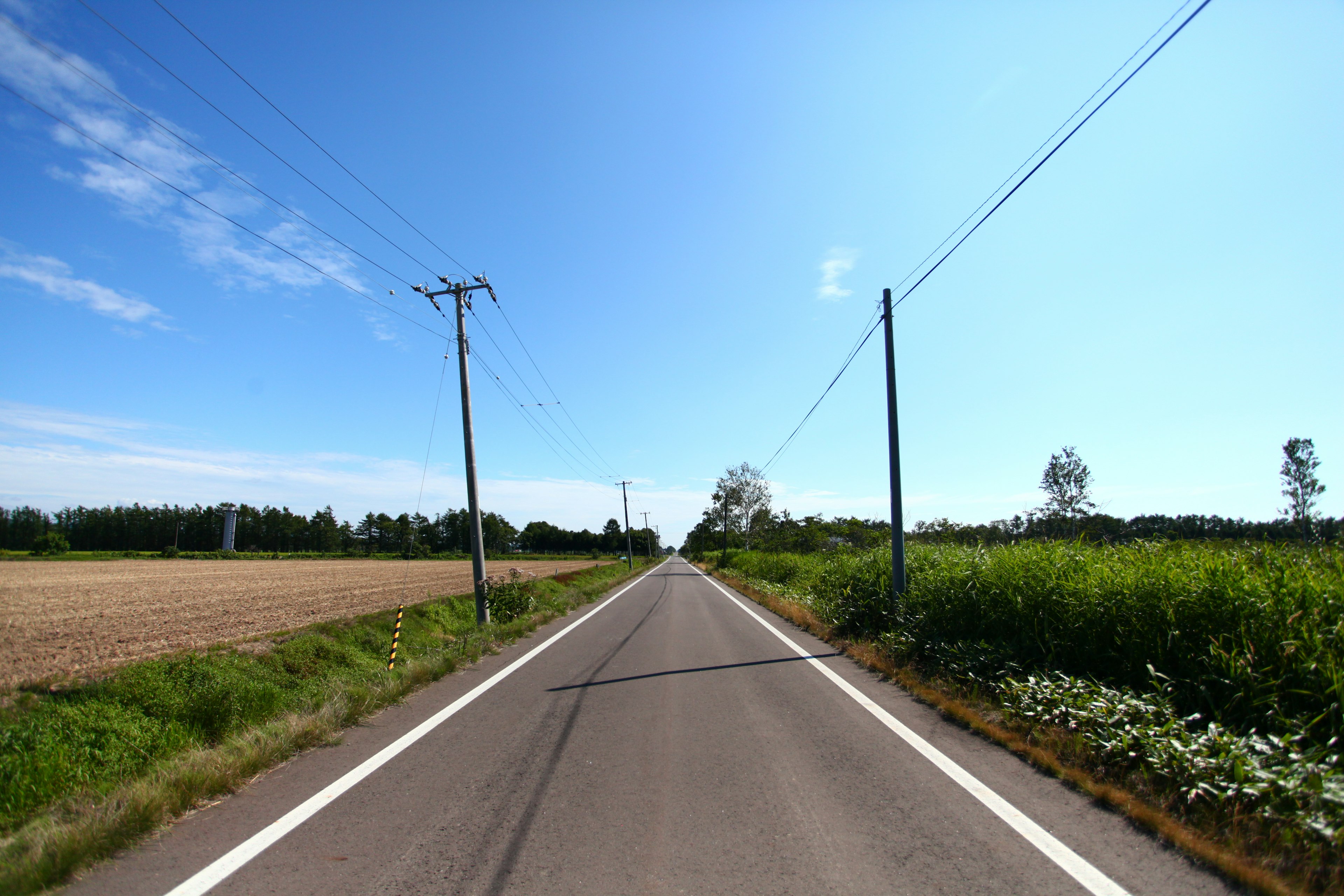 Straight road under a blue sky with surrounding landscape