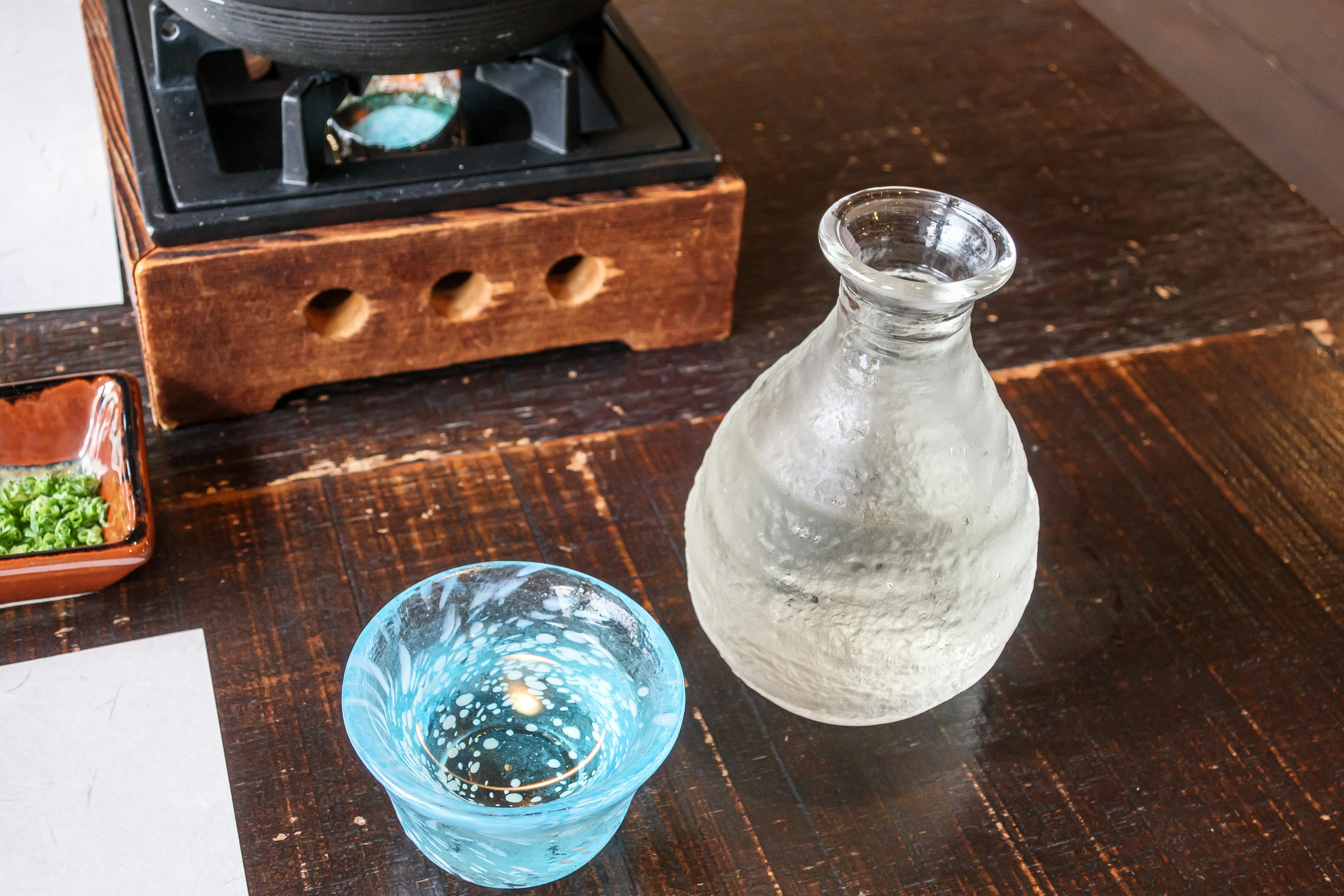 Una botella de sake y una copa de sake azul sobre una mesa de madera