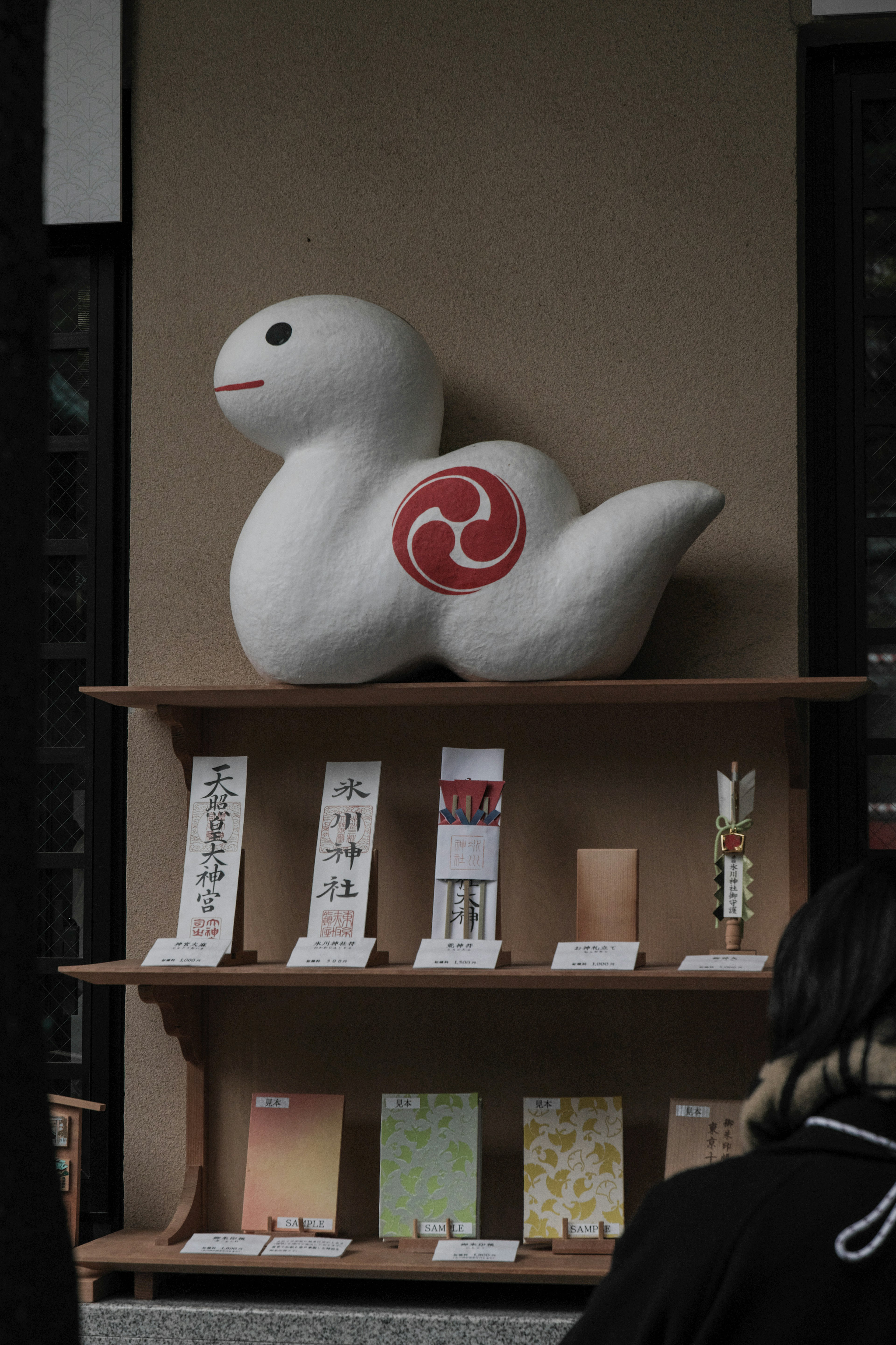 Estatua de animal blanco con diseño en espiral roja expuesta en una tienda con varios papeles tradicionales