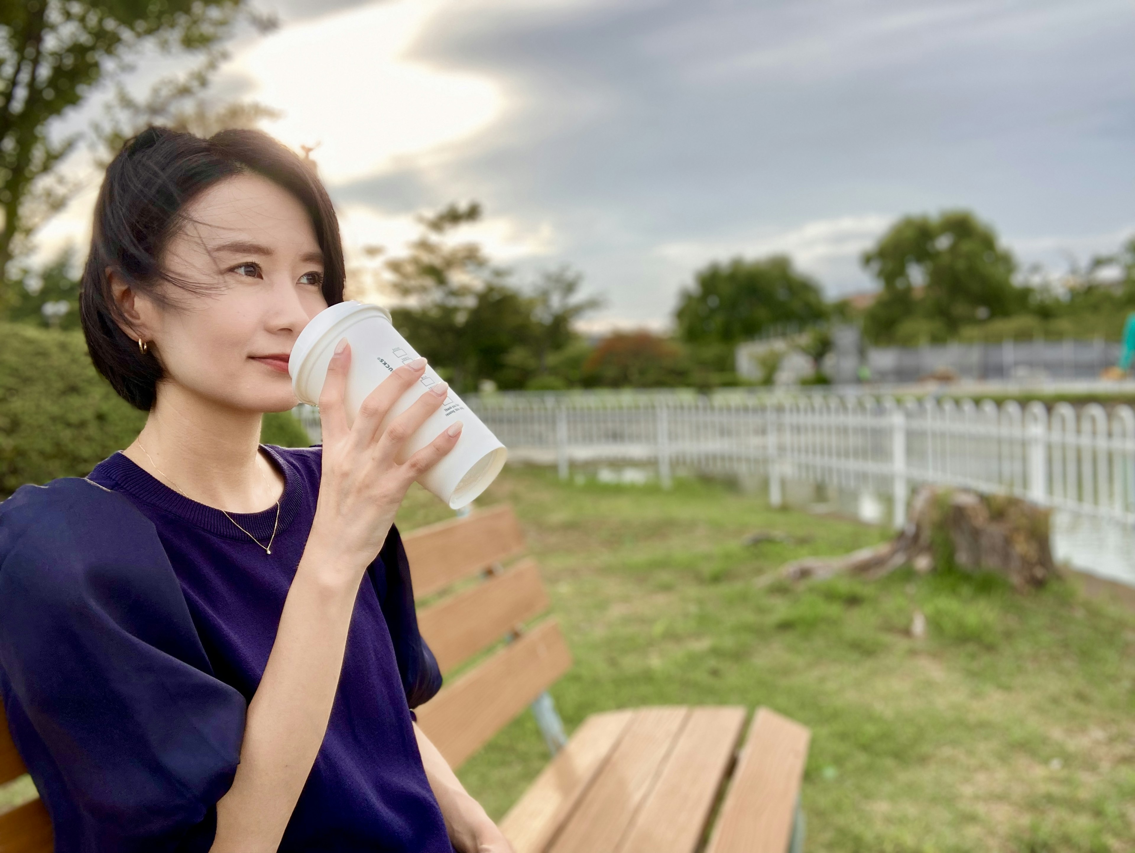 公園のベンチに座っている女性が飲み物を持っている