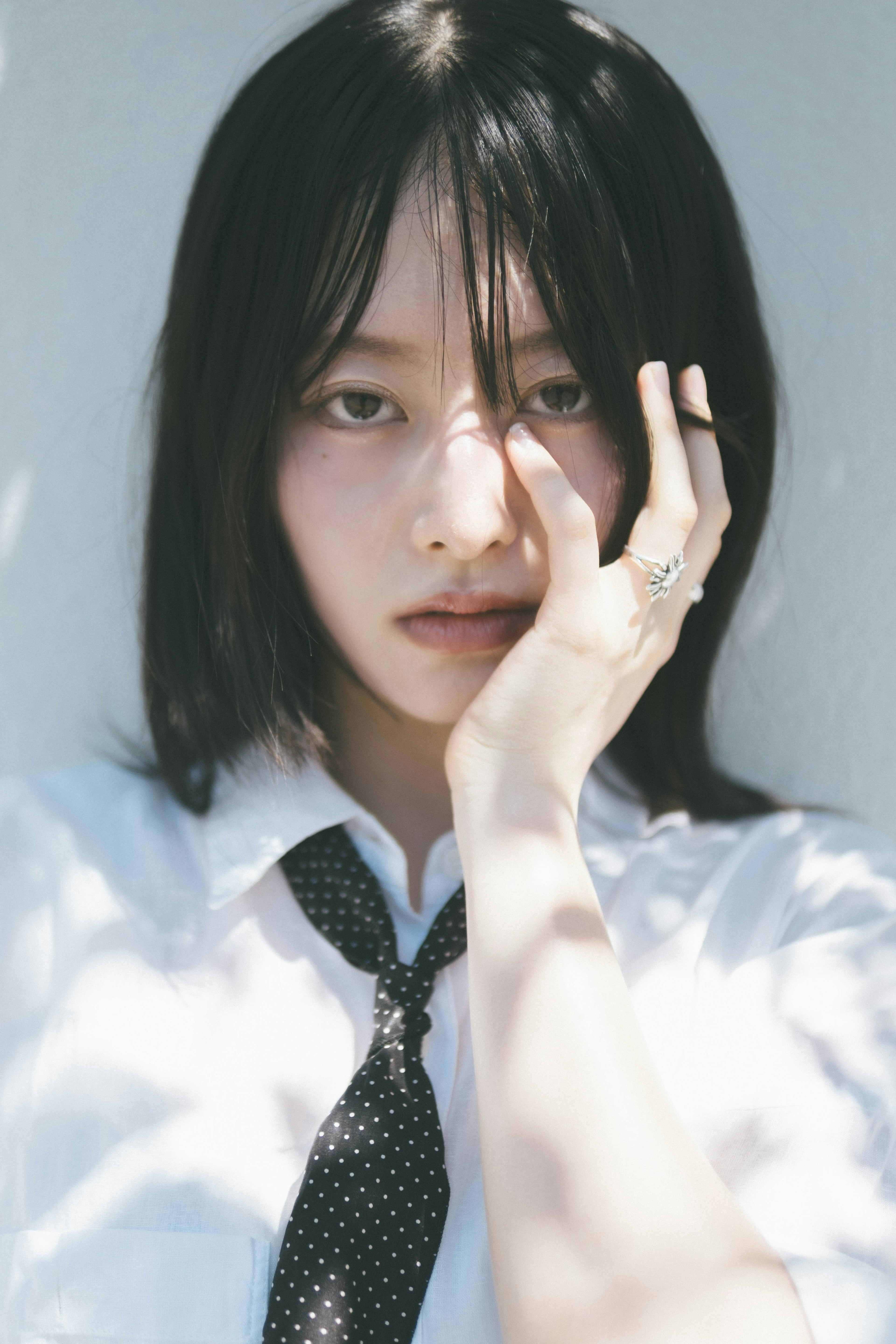 A woman in a white shirt gazing at the camera while partially covering her face with her hand