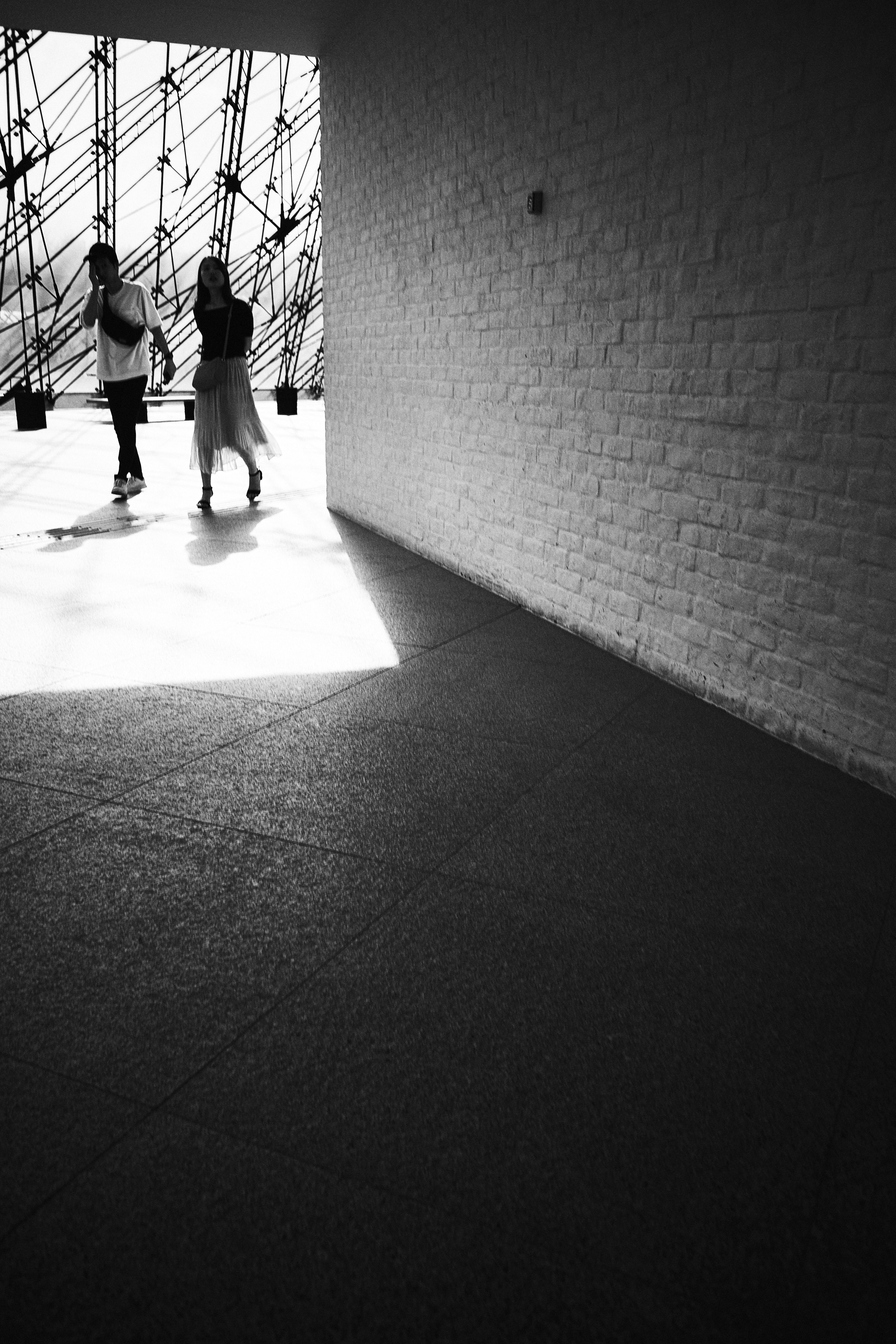 Two people walking through a dimly lit corridor in black and white