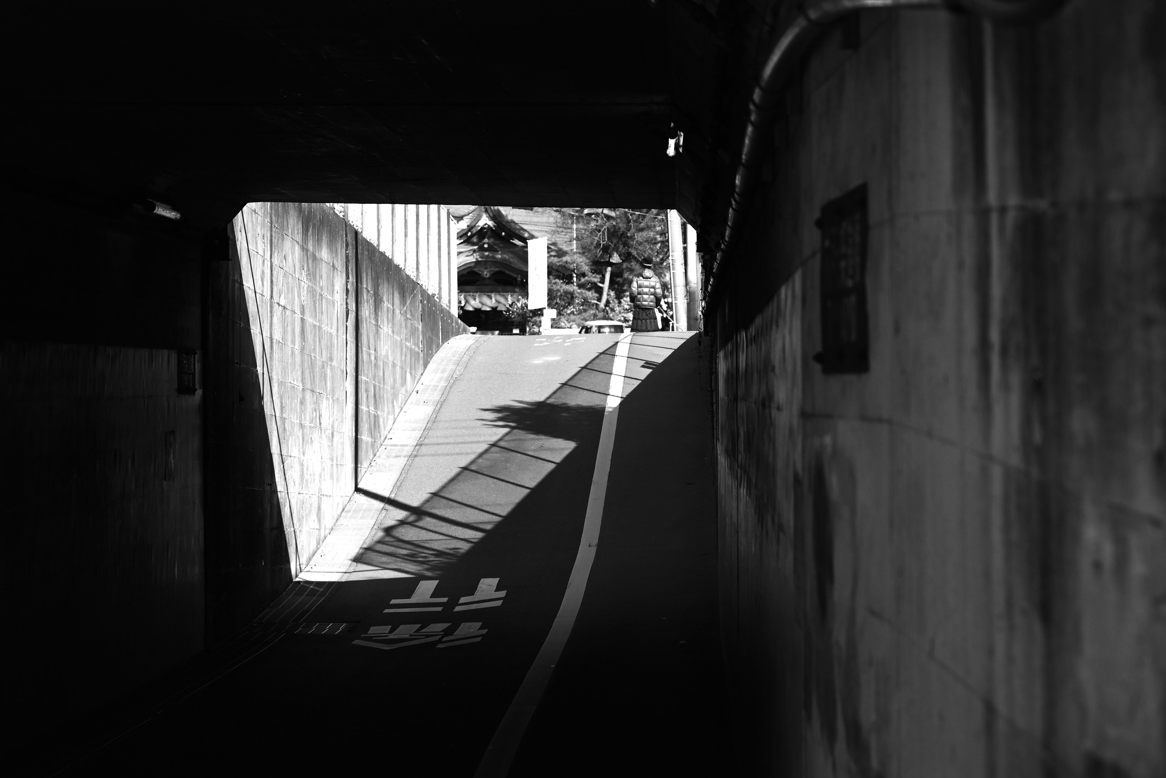 Black and white image of a tunnel with a sloped road and distinct shadows