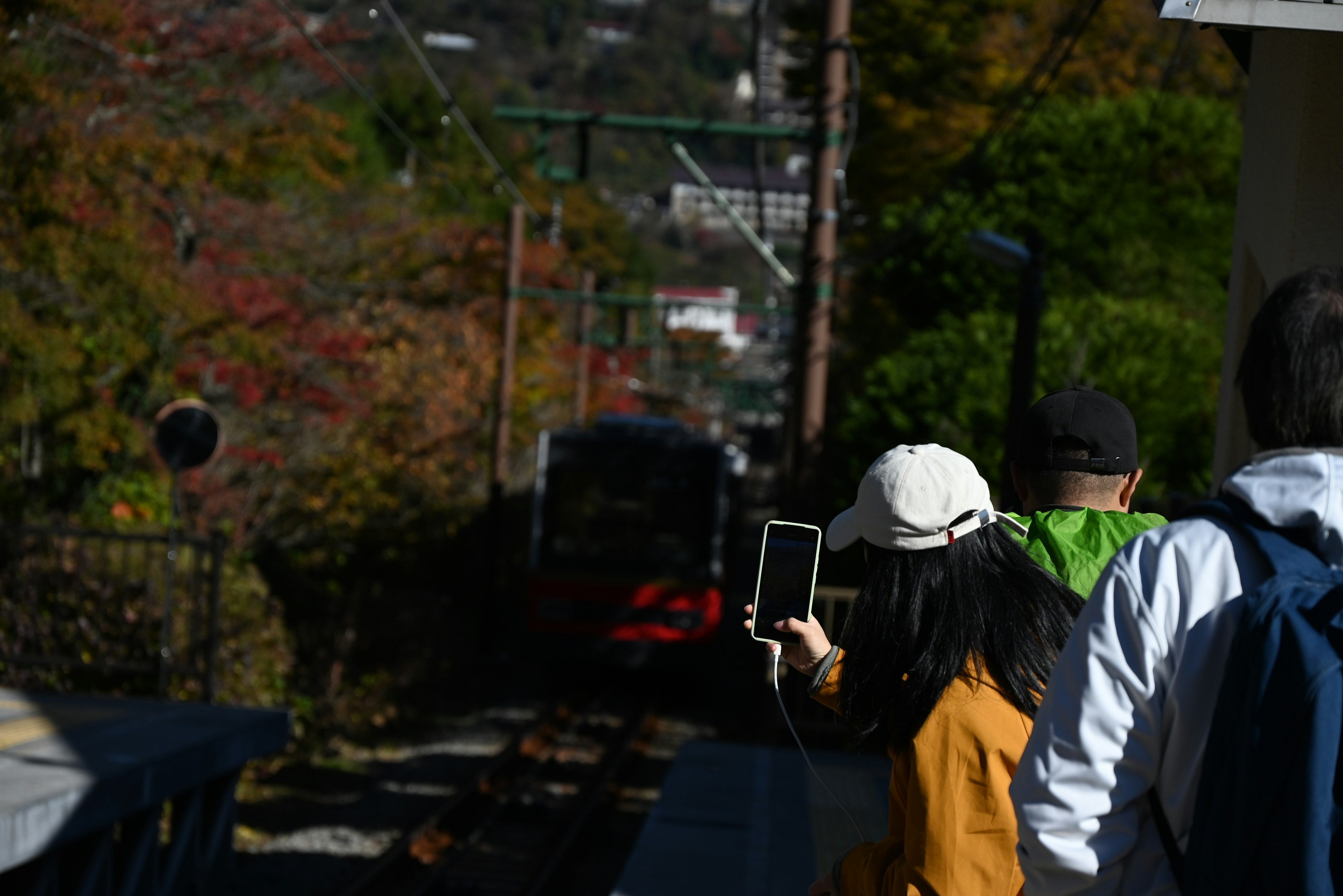 Personas esperando un tren en un paisaje otoñal con una mujer sosteniendo un smartphone