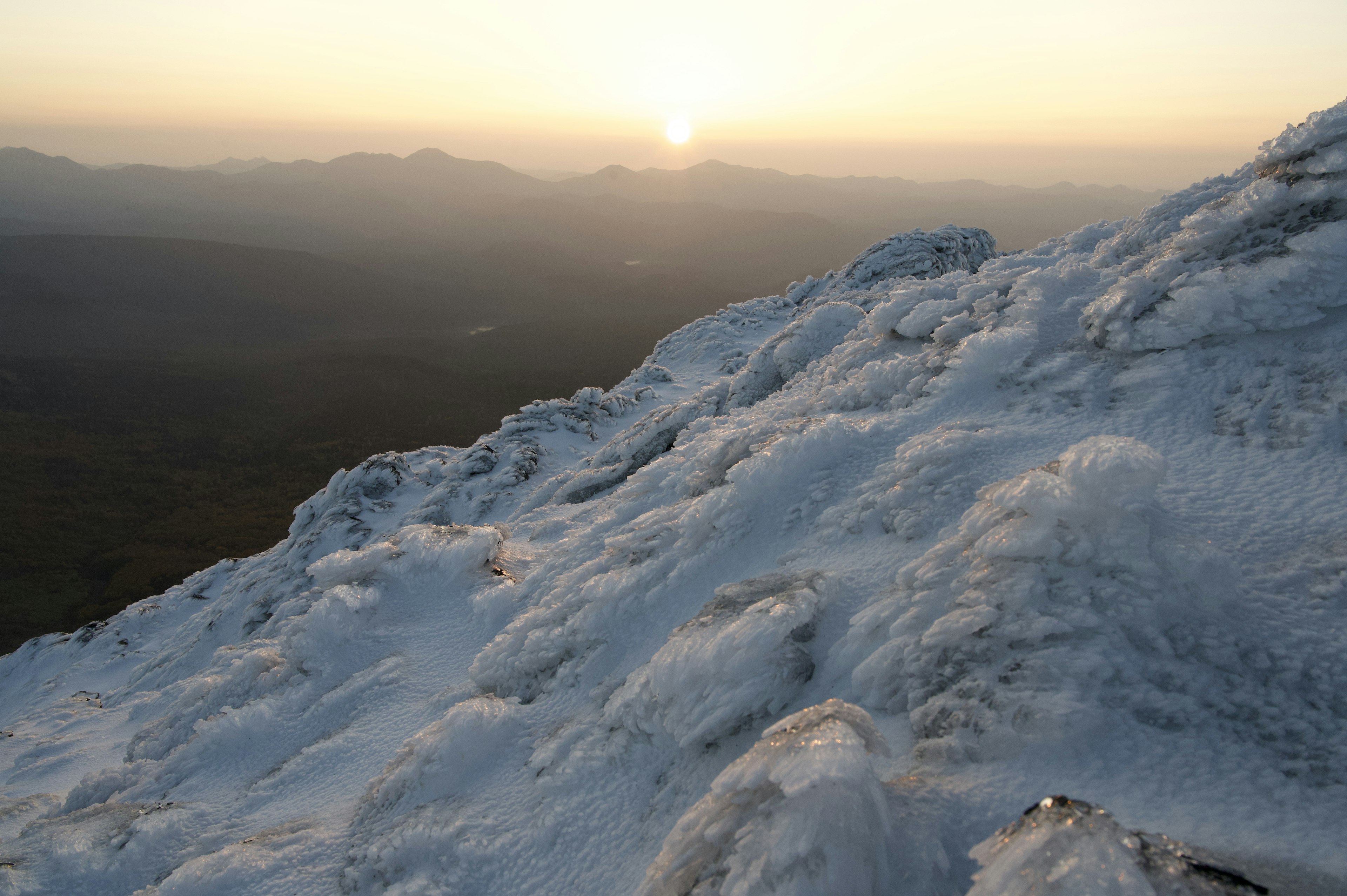 山の頂上からの雪に覆われた風景と日の出の光