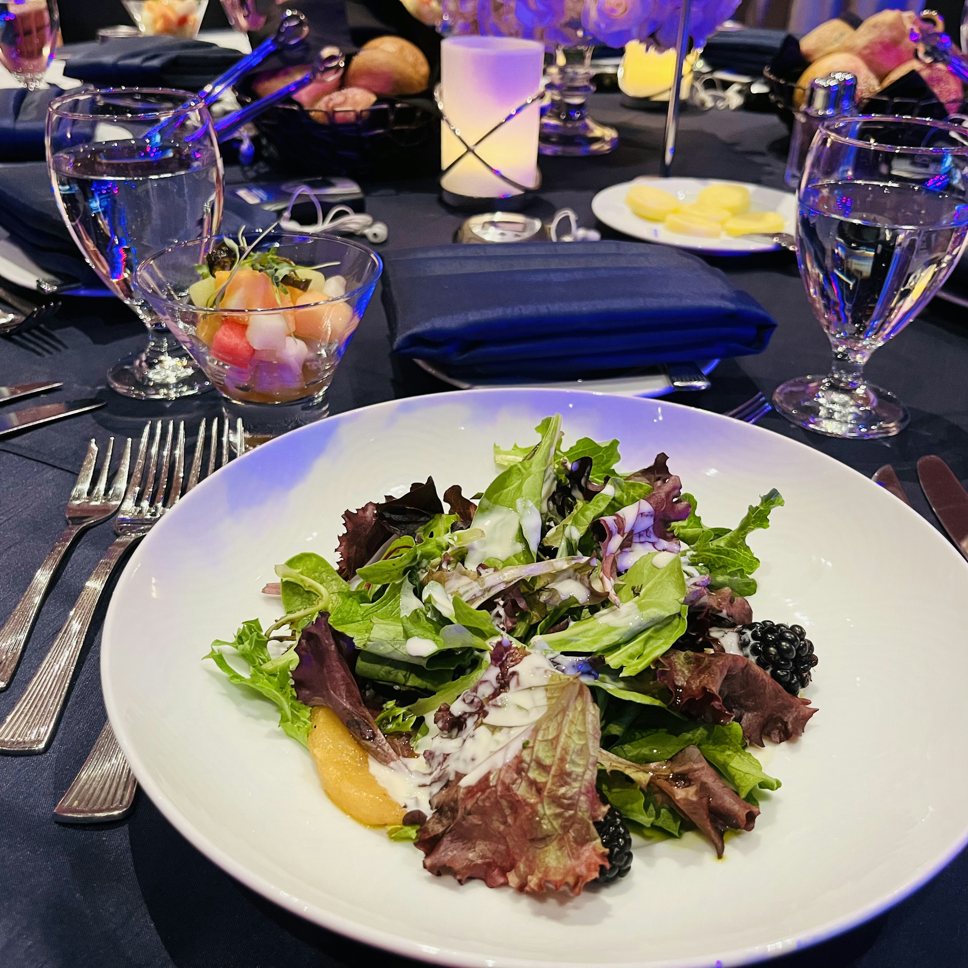 A beautifully arranged salad on a white plate with elegant table setting