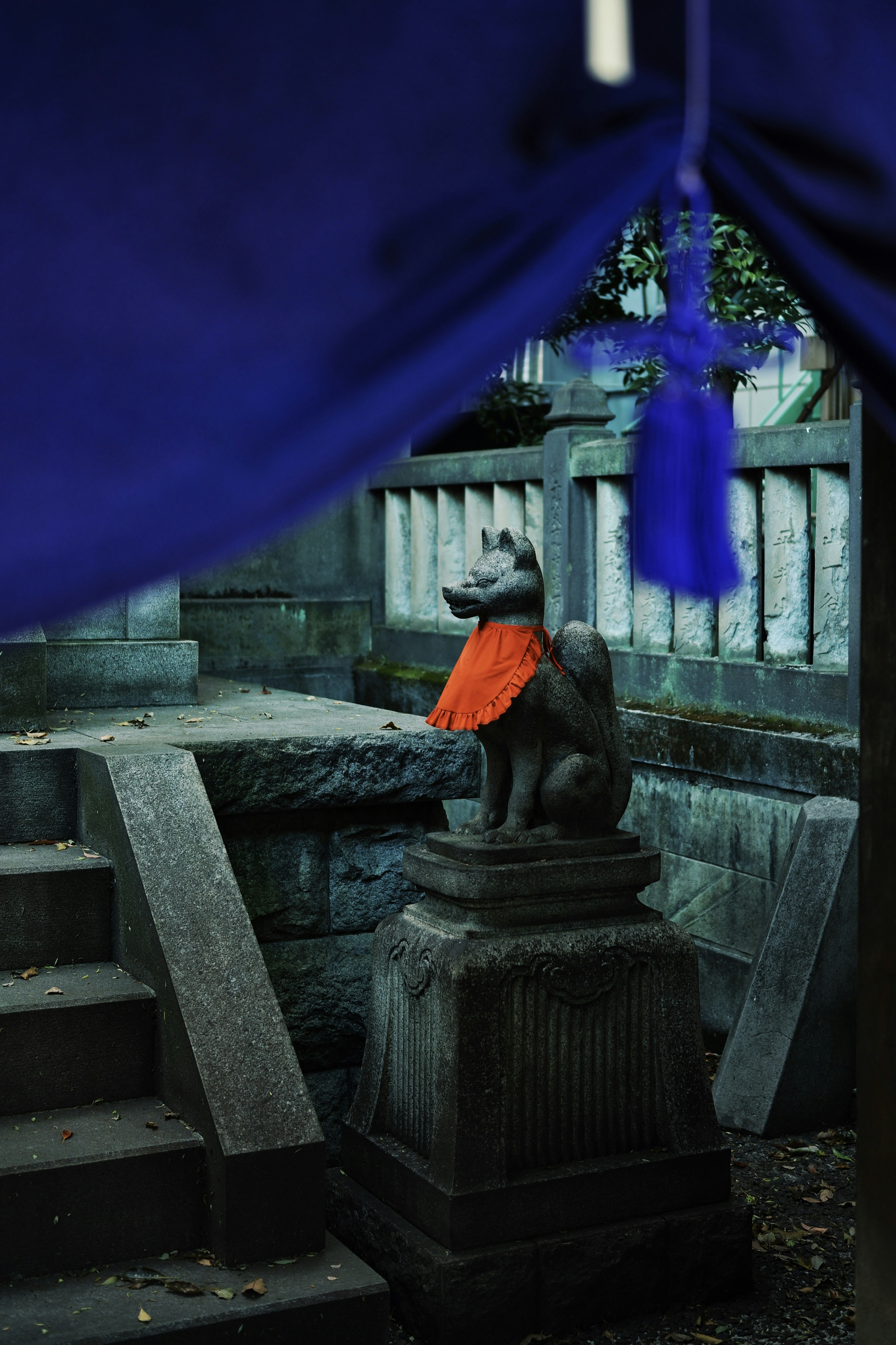 Estatua de león guardián de piedra con una bufanda naranja debajo de un tejido azul