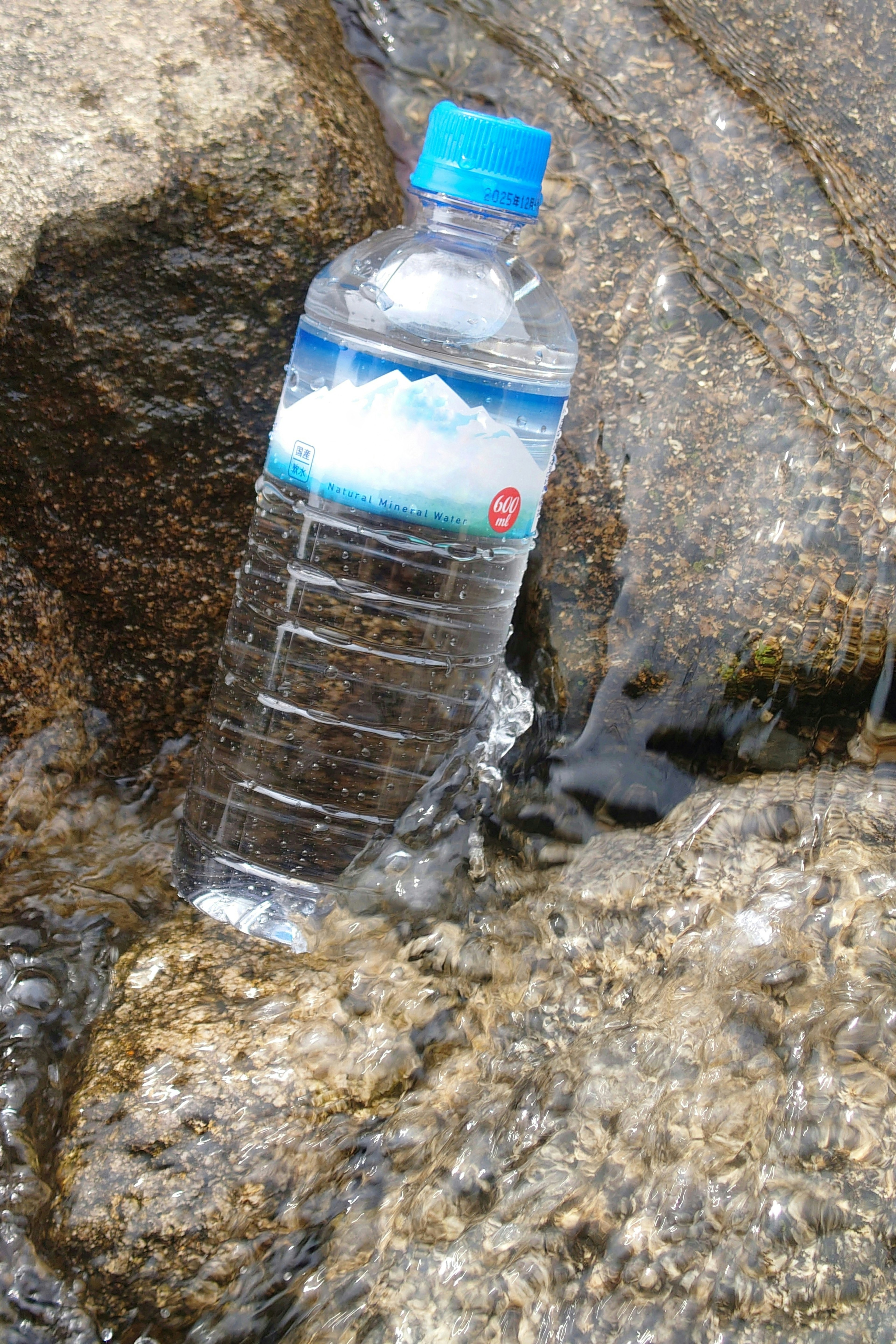 Bild einer Wasserflasche, die in fließendem Wasser zwischen Steinen liegt