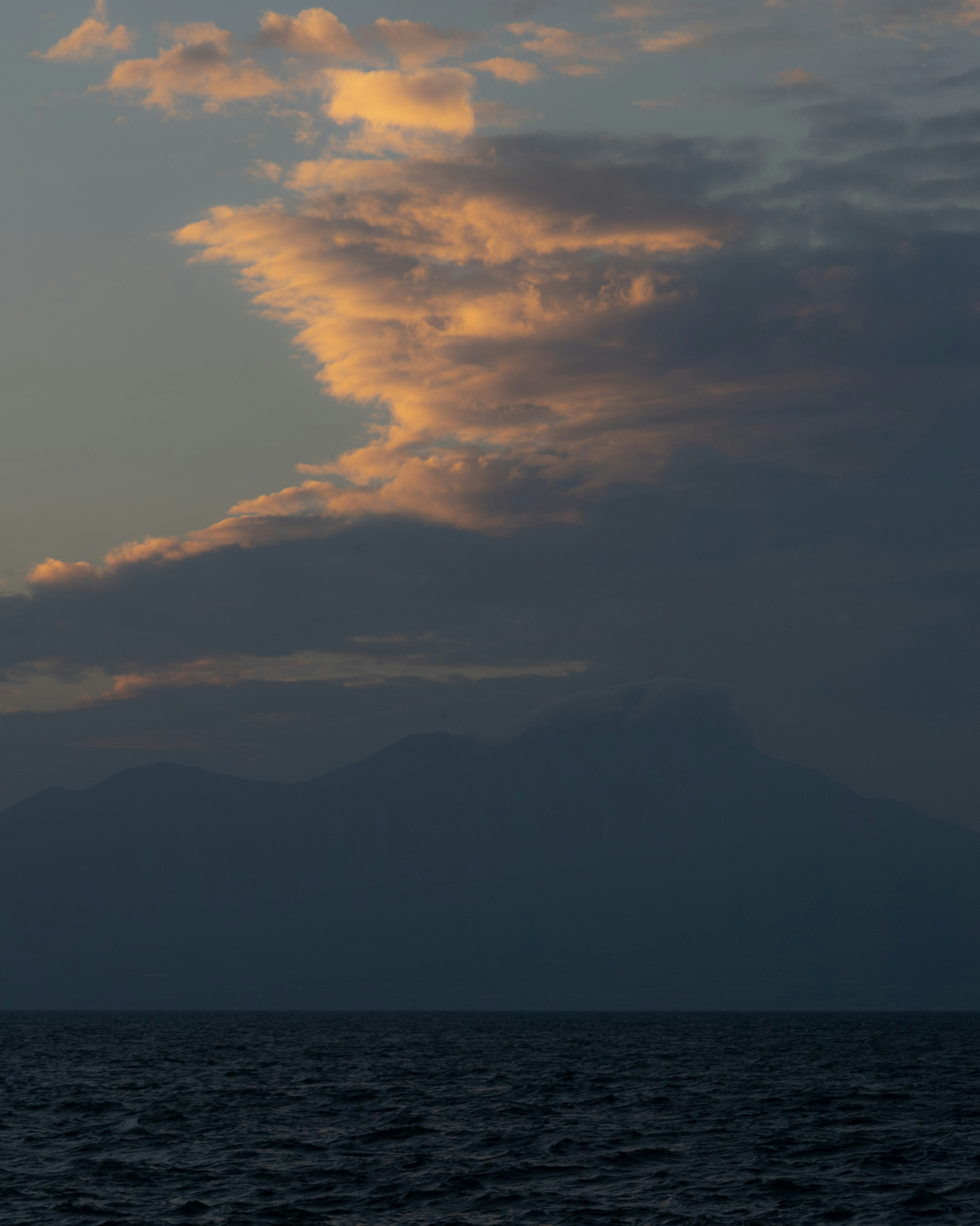 Silhouette von Bergen und Wolken über dem Meer bei Sonnenuntergang