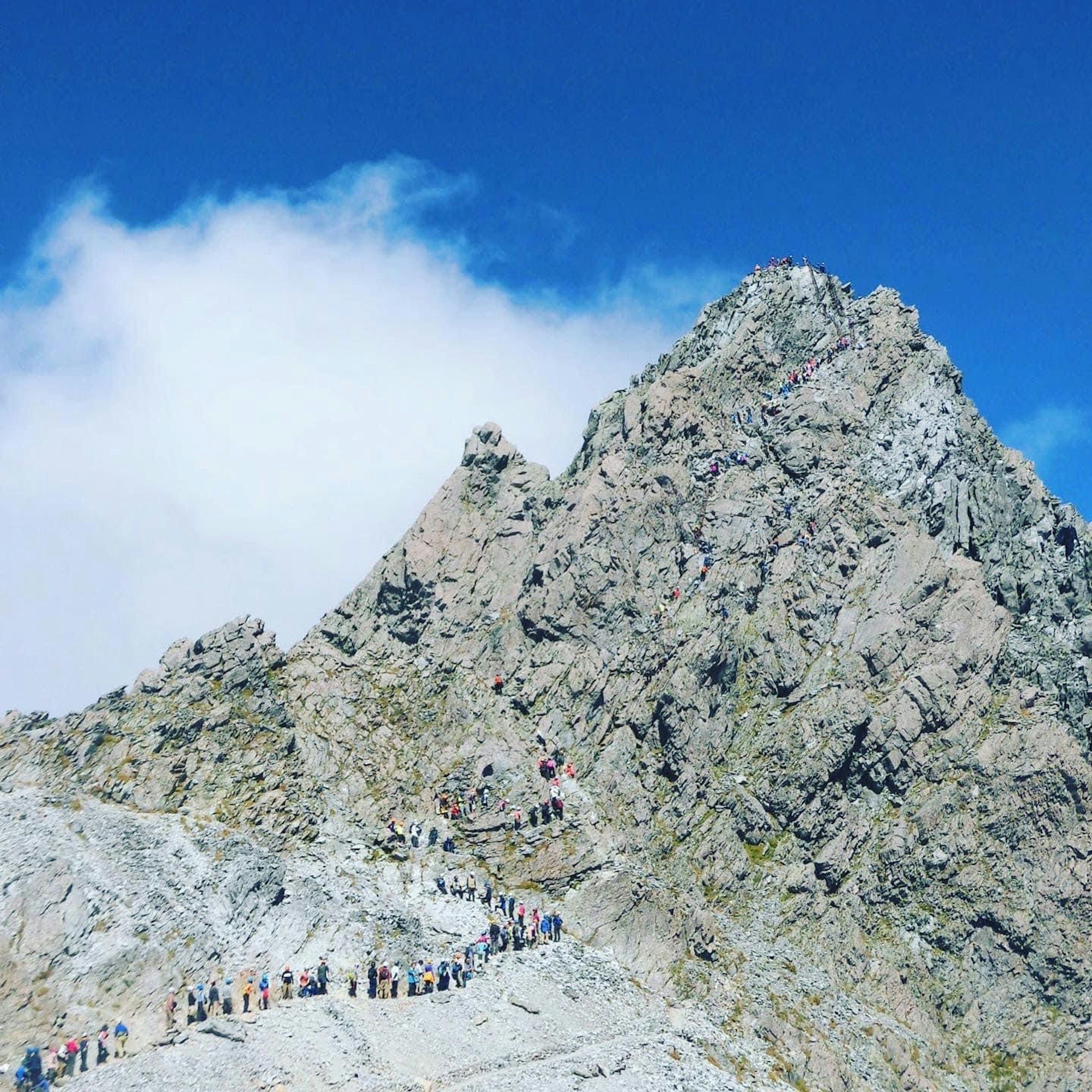 Senderistas en un sendero montañoso rocoso bajo un cielo azul claro