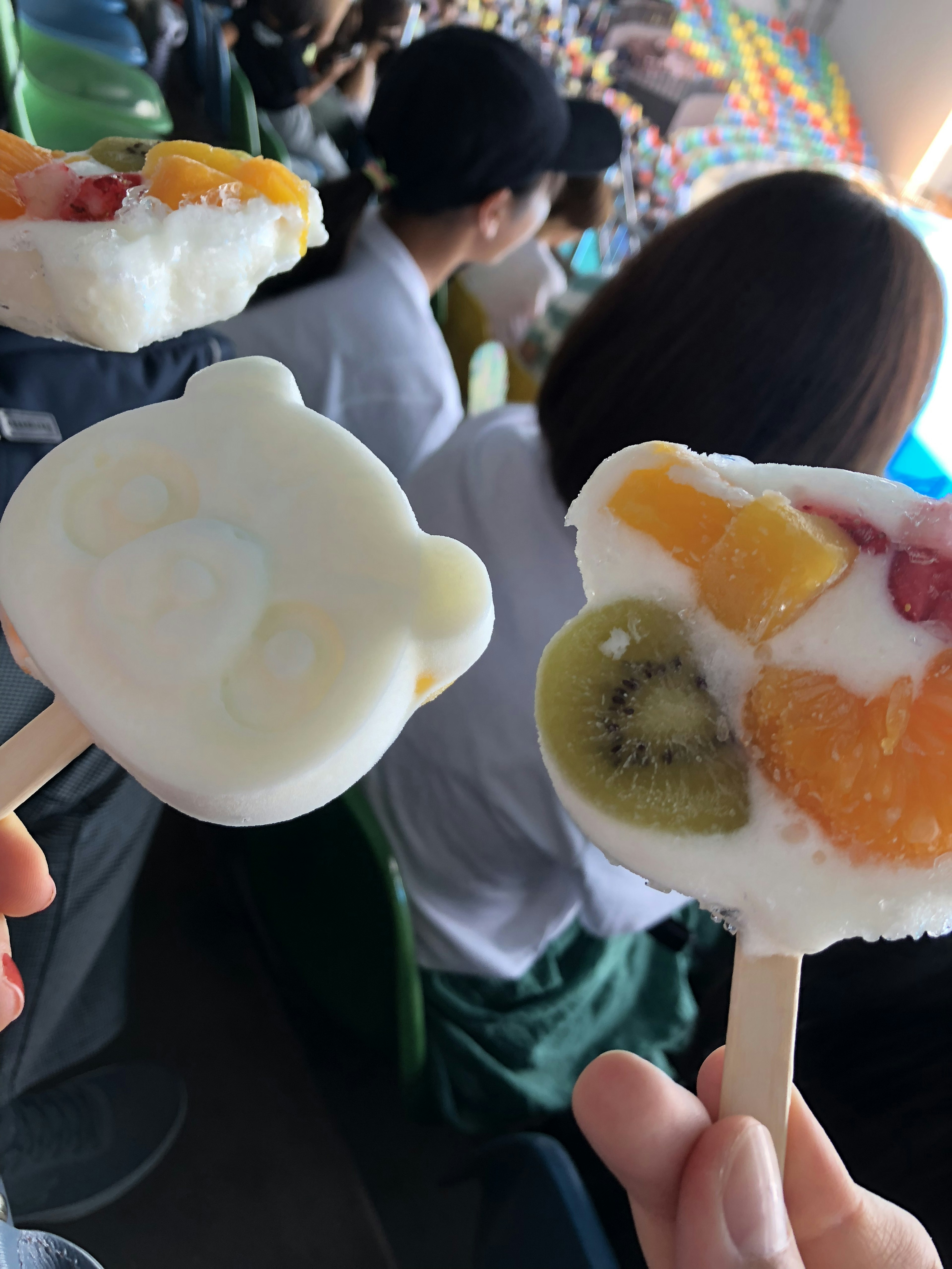 Due ghiaccioli colorati tenuti da mani con guarnizioni di frutta