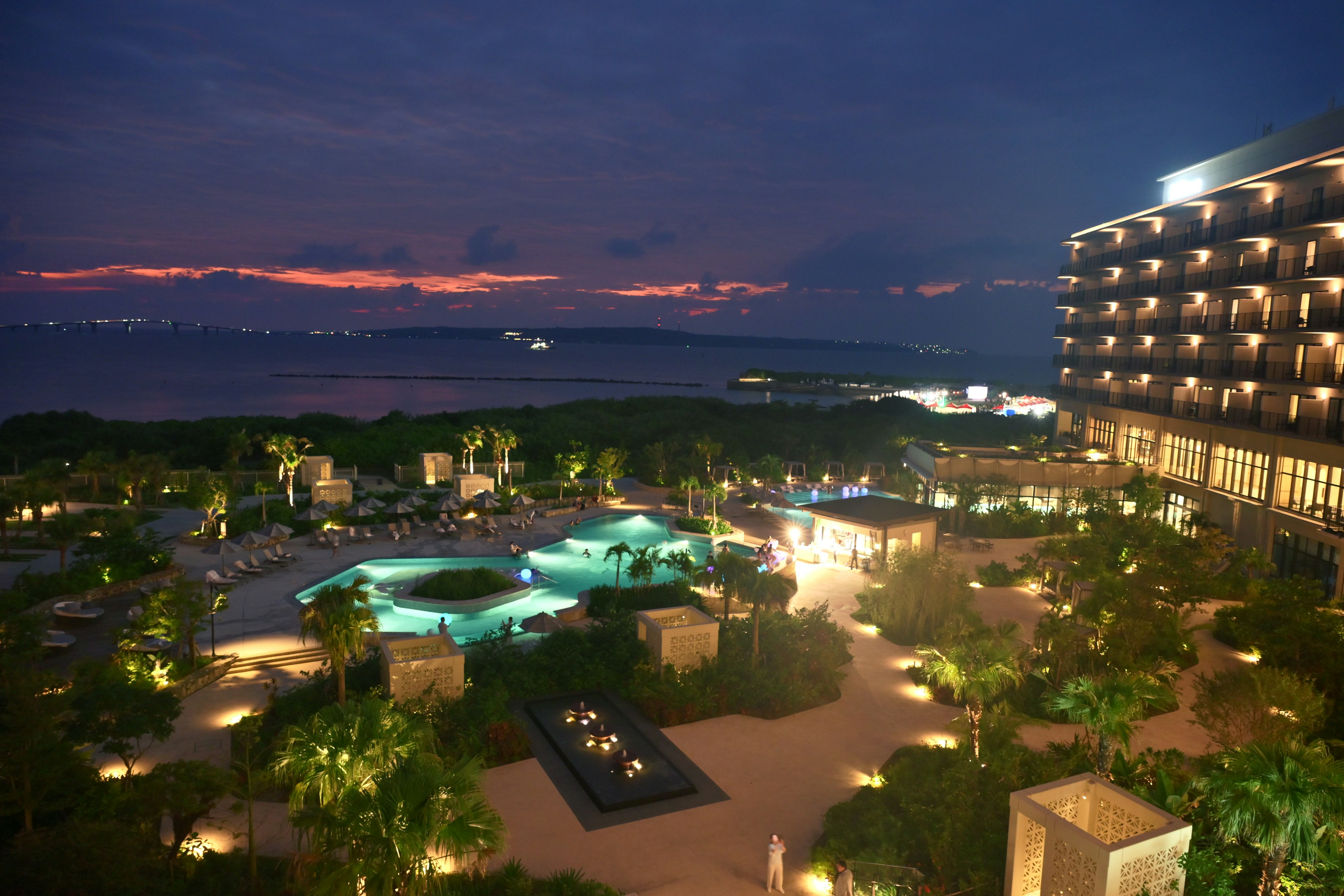 Vista notturna di un resort con piscine illuminate e giardini lussureggianti che si affacciano sul mare