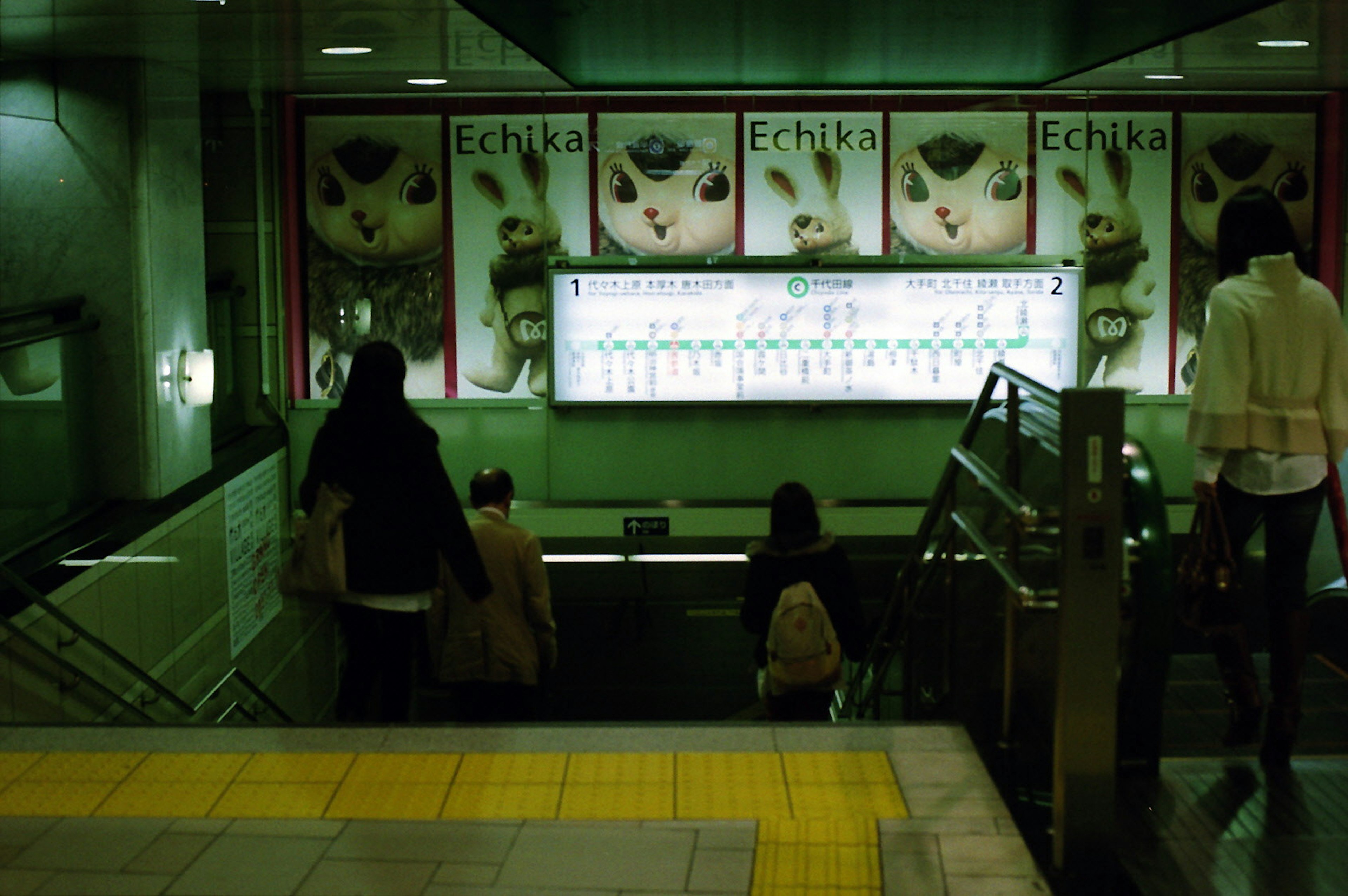 Persone che scendono verso una stazione della metropolitana con illuminazione verde e pubblicità