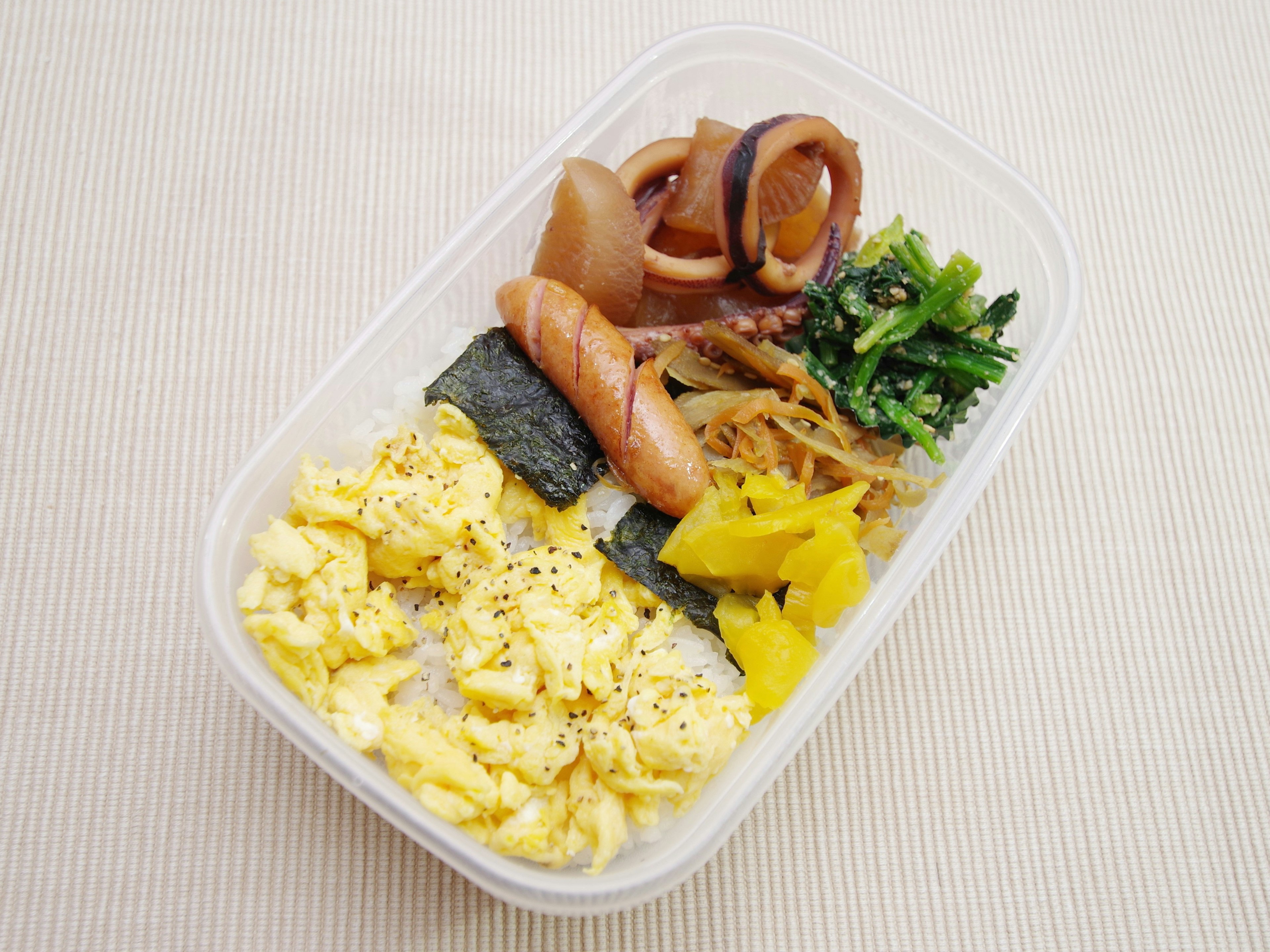 Caja bento con huevos revueltos, alga, salchichas y verduras en escabeche