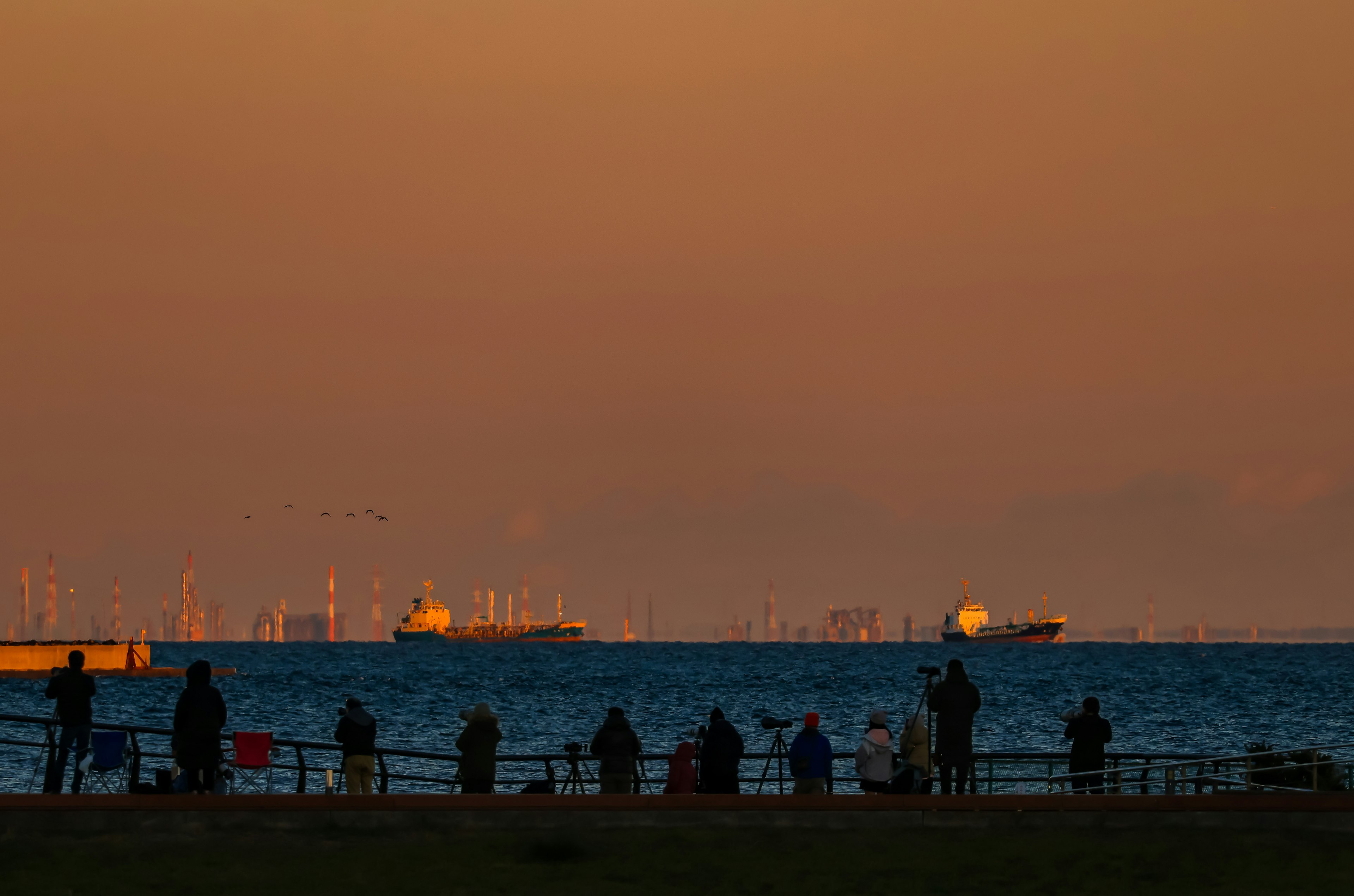 夕焼けの海を背景に立つ人々と貨物船のシルエット