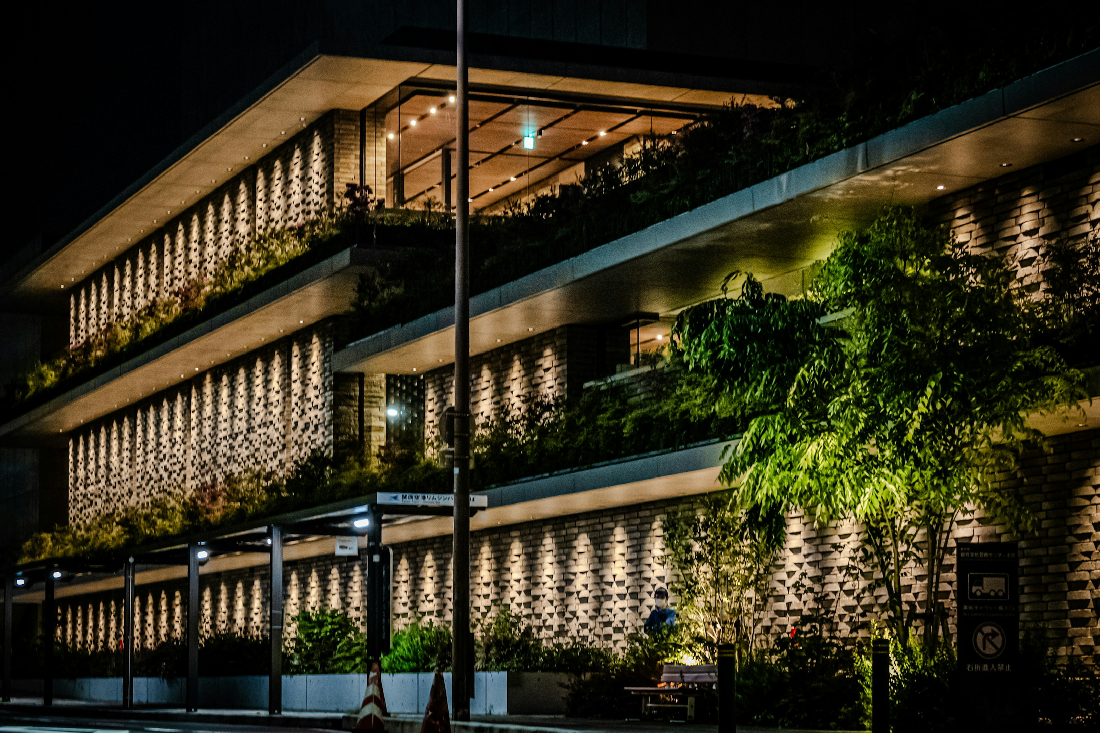 Exterior de un edificio moderno bellamente iluminado por la noche con plantas exuberantes en los balcones y paredes de piedra